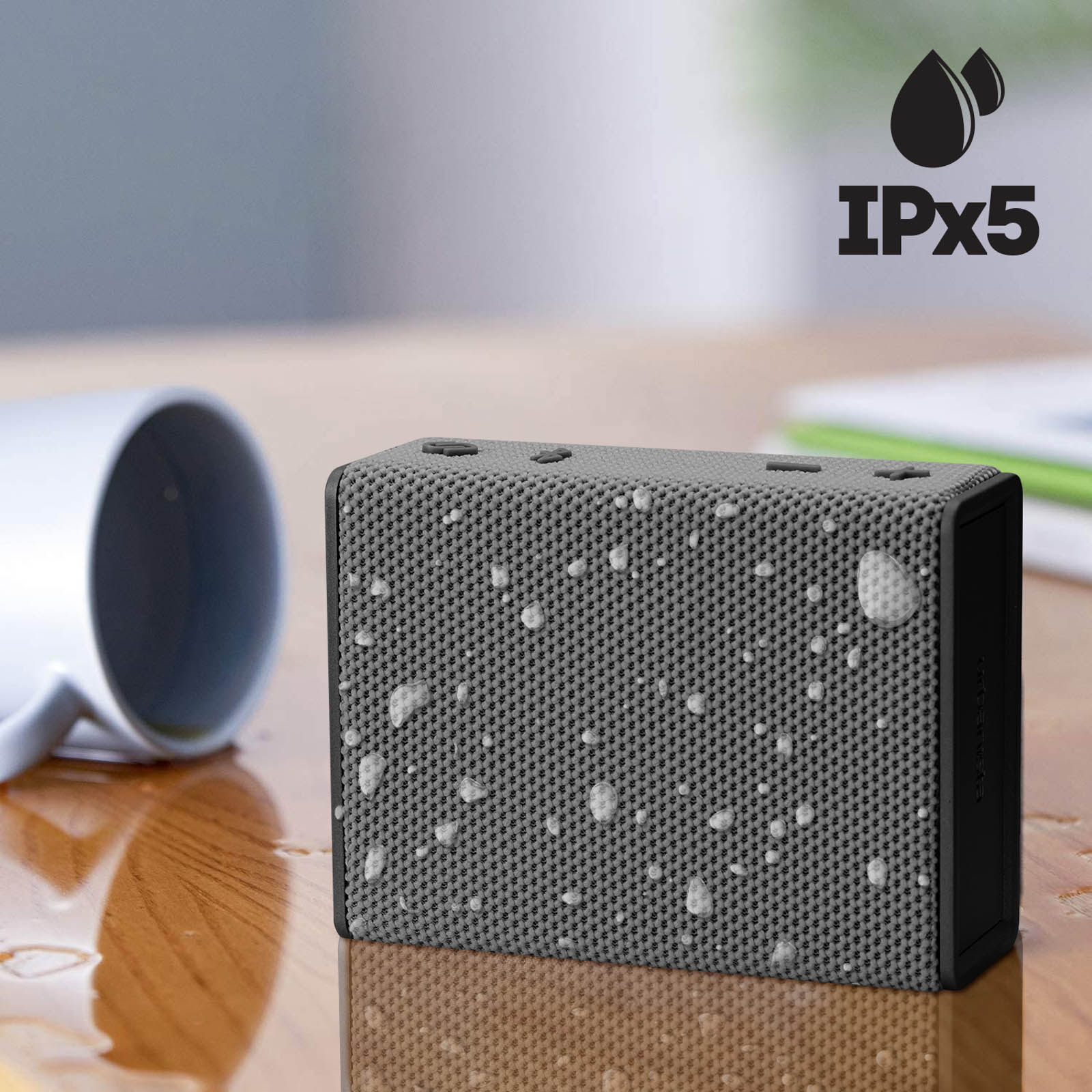 Szary głośnik z kroplami wody na drewnianym stole z etykietą IPX5.