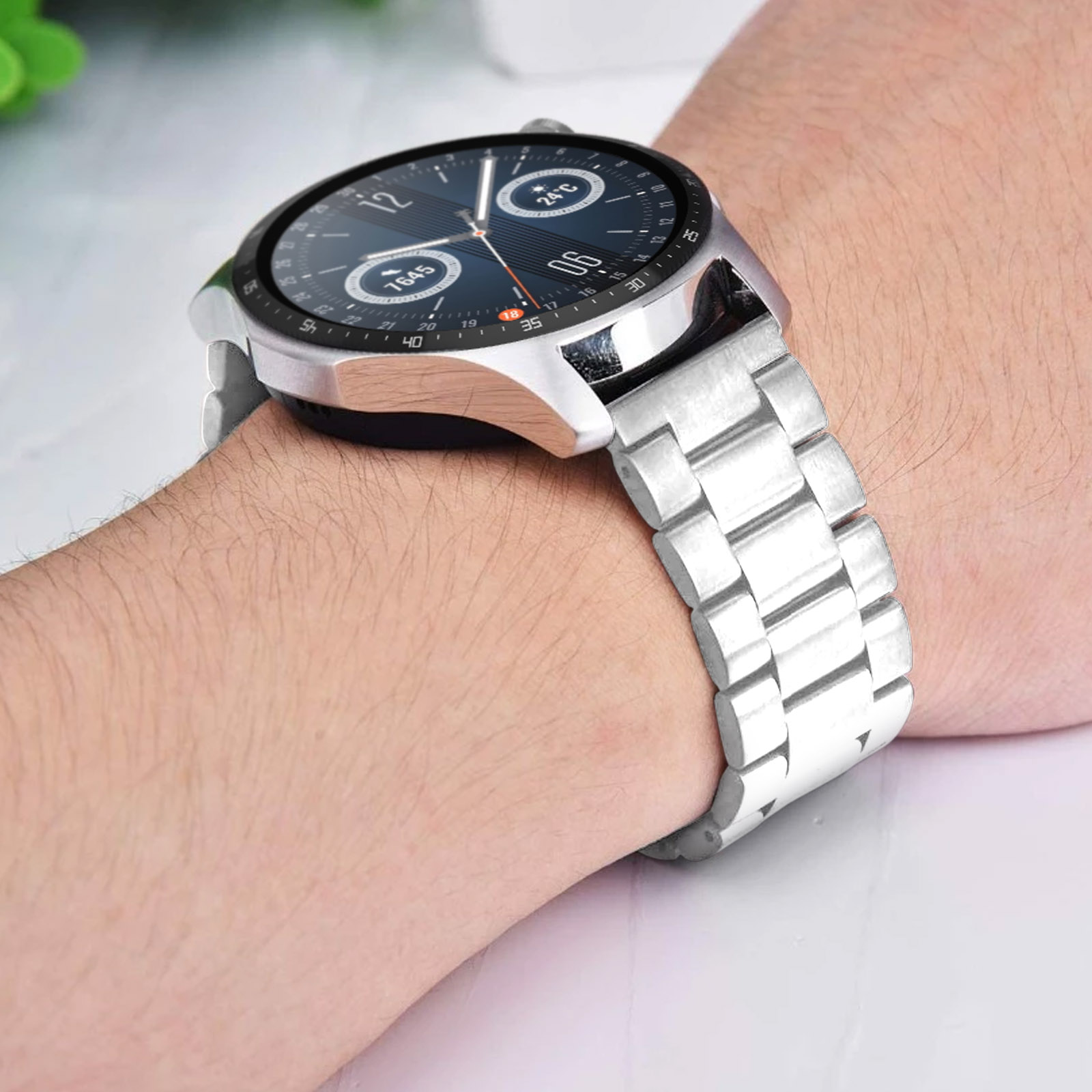 Un reloj inteligente plateado en una muñeca con correa plateada. La esfera muestra hora y temperatura.