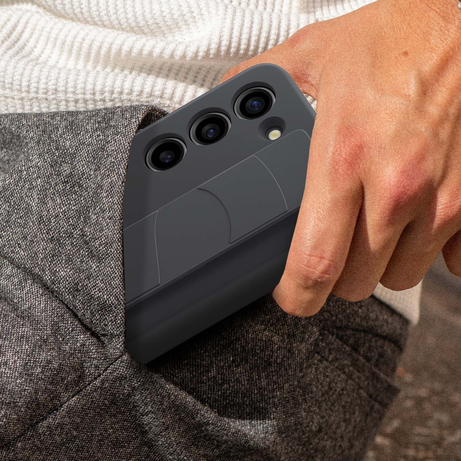 Osoba trzymająca ciemnoszary telefon w kieszeni. Telefon ma trzy aparaty i pasek.