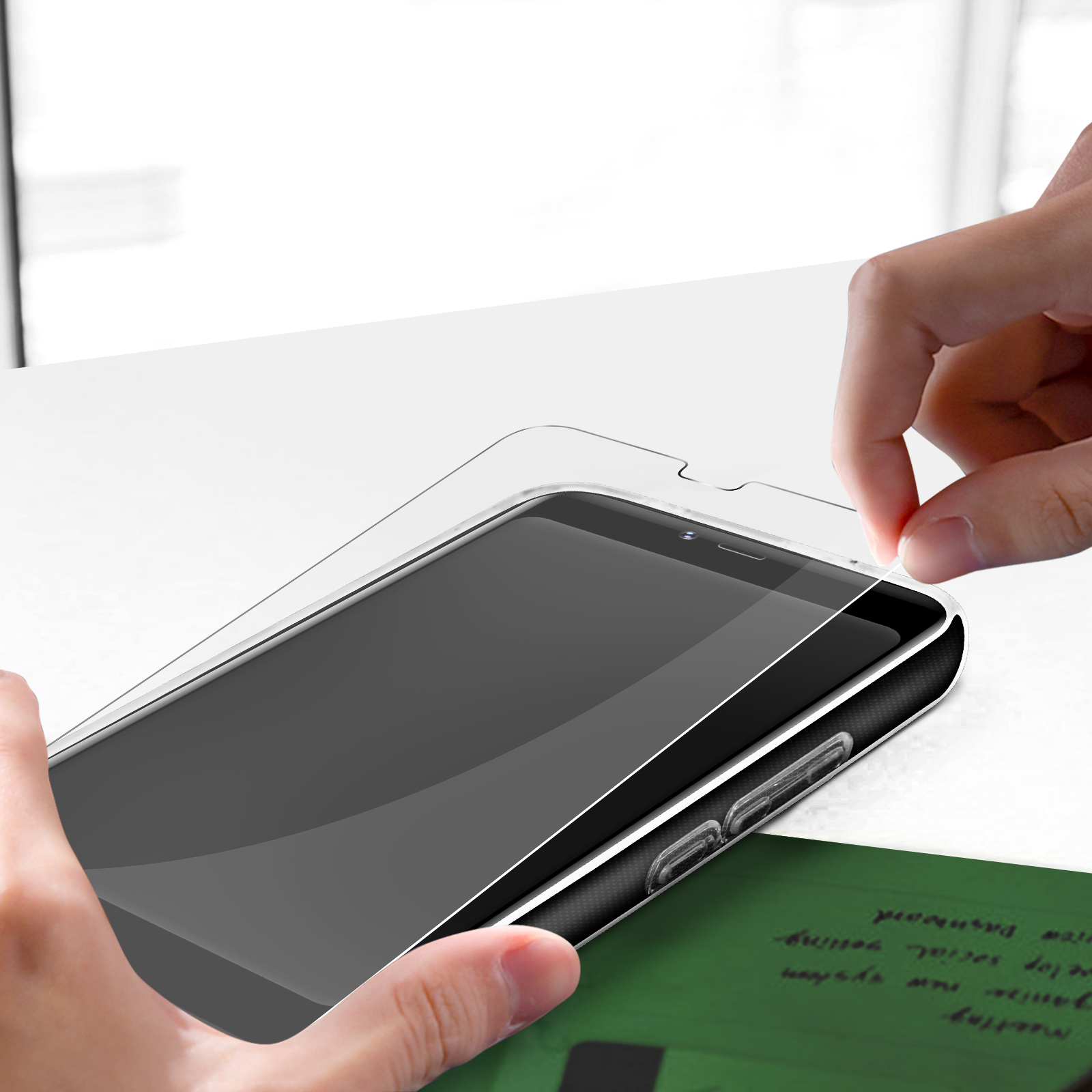 Hand platziert eine Displayschutzfolie auf einem Smartphone. Das Telefon liegt auf weißer Oberfläche.