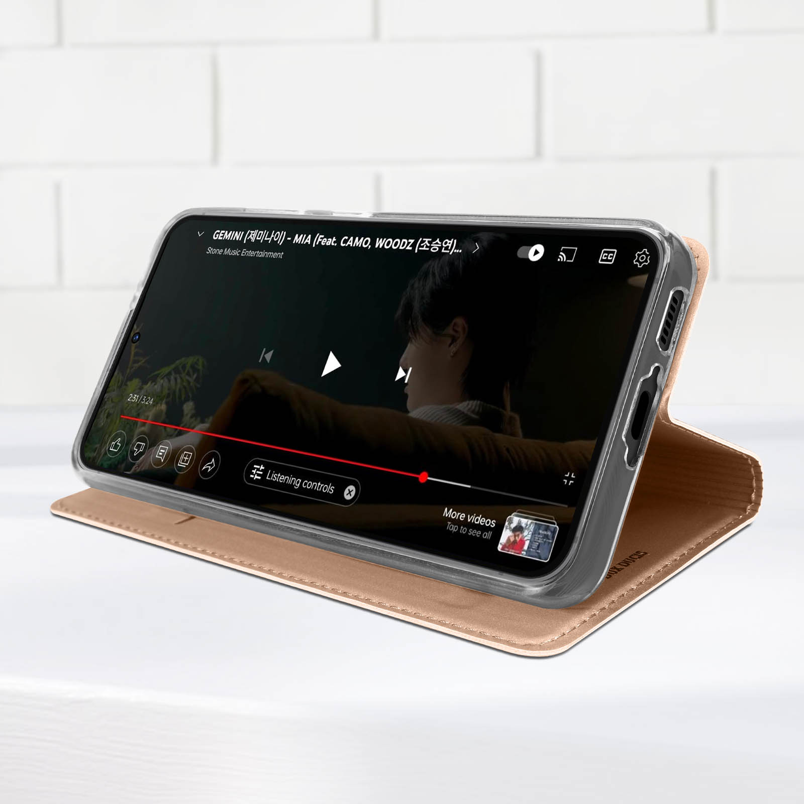 Telefon zeigt Video, in beiger Hülle, auf weißem Tisch, nahe weißer Wand.