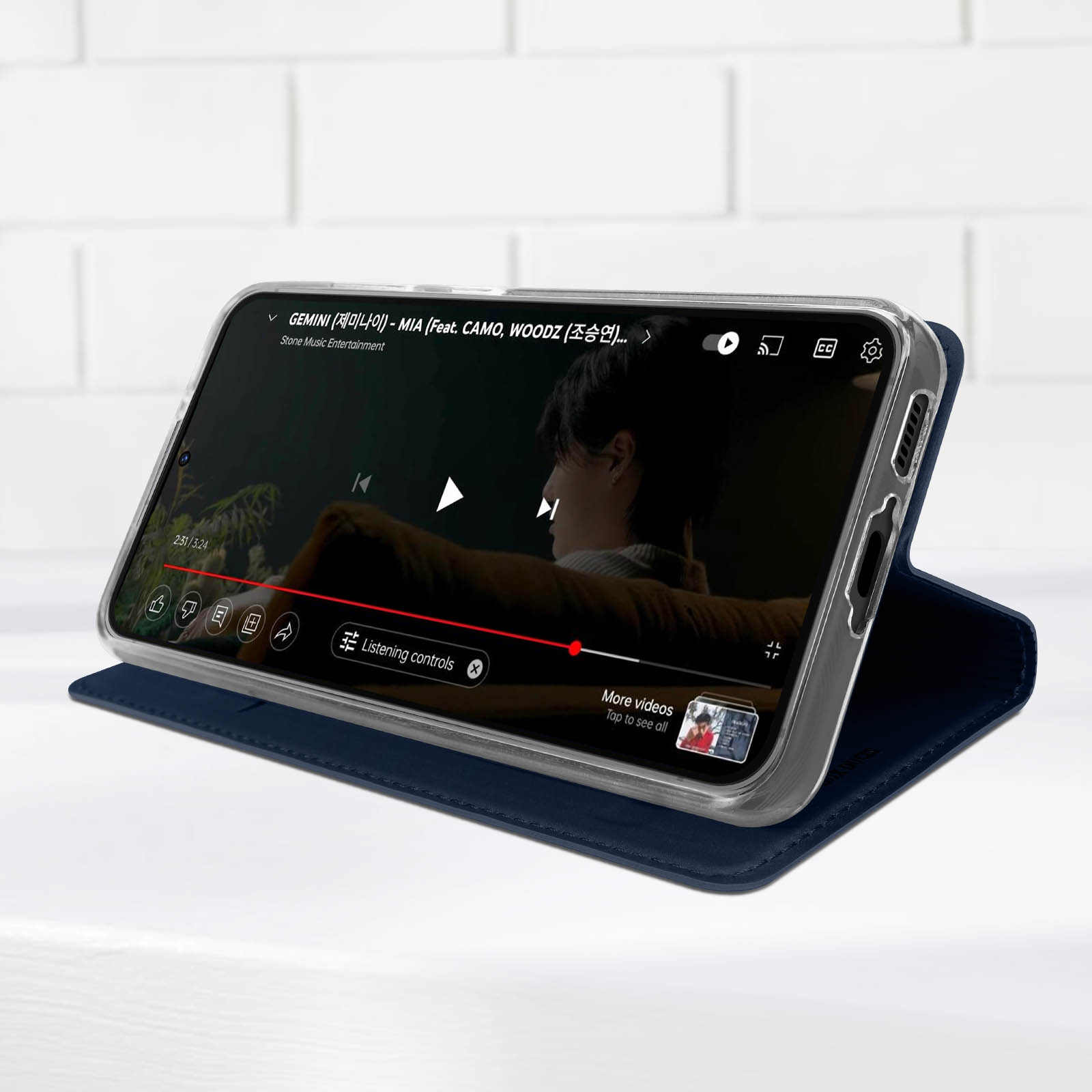 Téléphone sur un support jouant une vidéo. L'étui est bleu marine. Un bouton de lecture est visible.