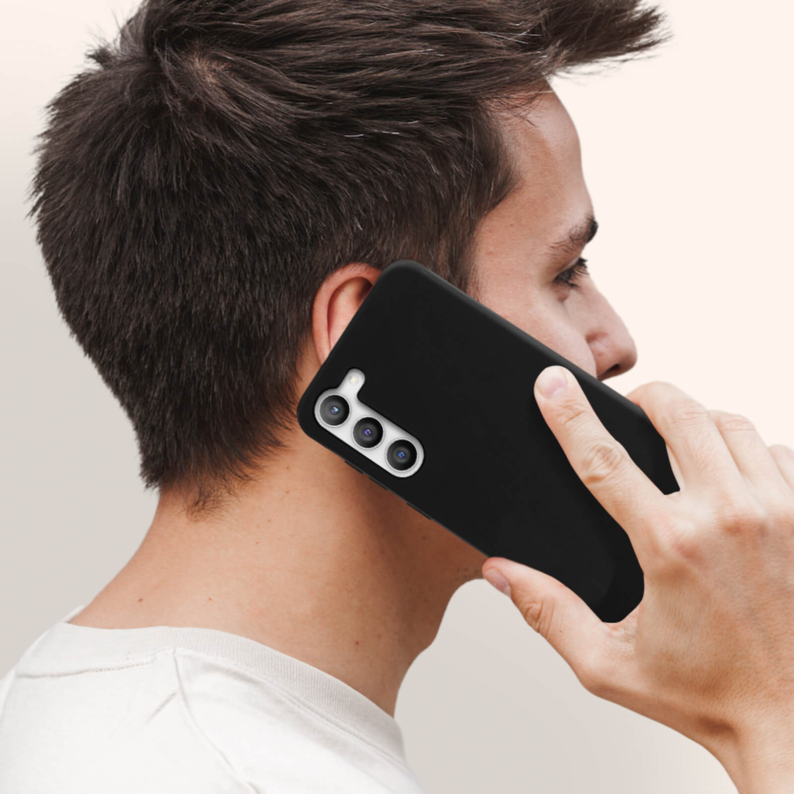 Mann hält ein schwarzes Telefon mit schwarzer Hülle ans Ohr. Kamera ist fokussiert.