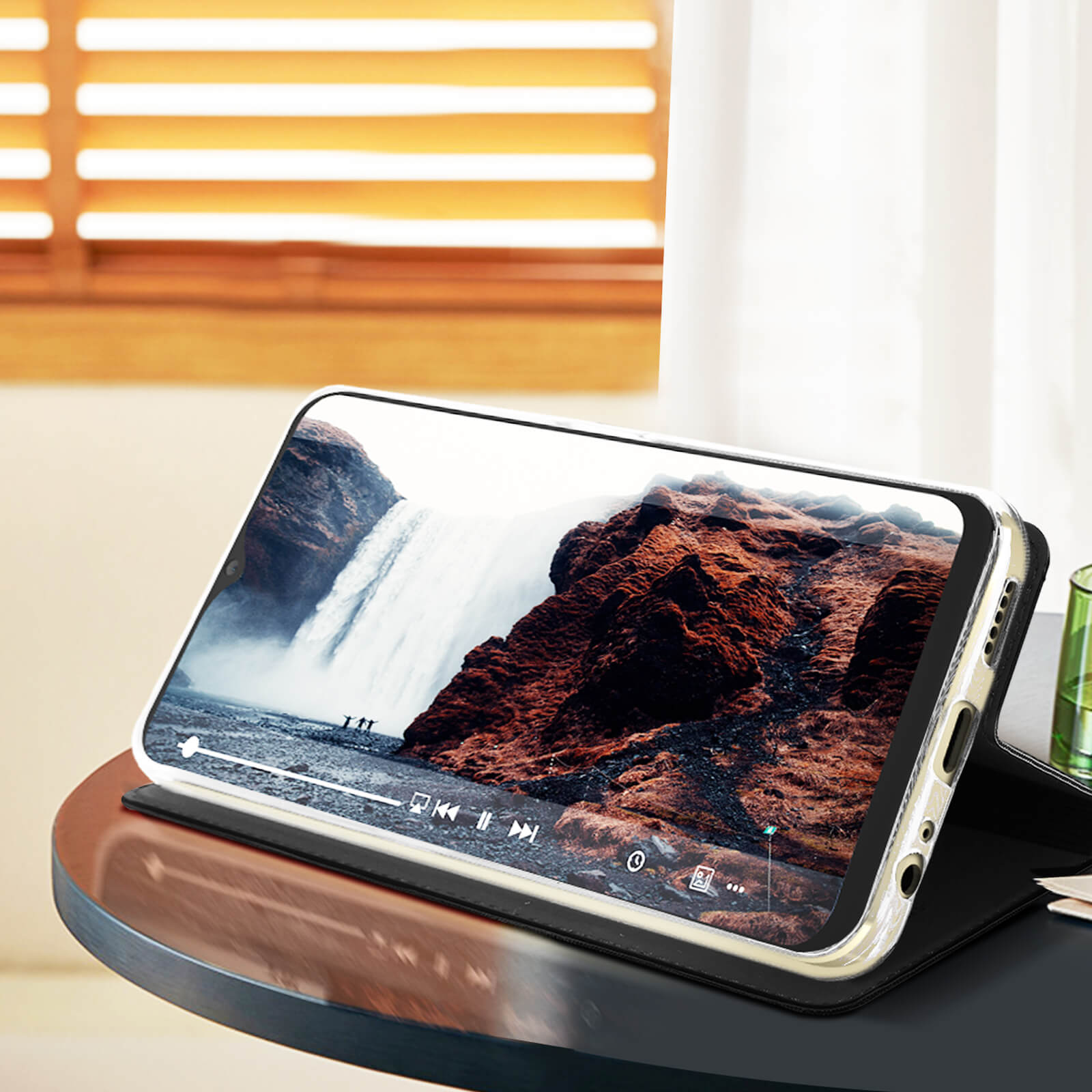 Telefono in una custodia che riproduce un video di una cascata. Su un tavolo scuro.