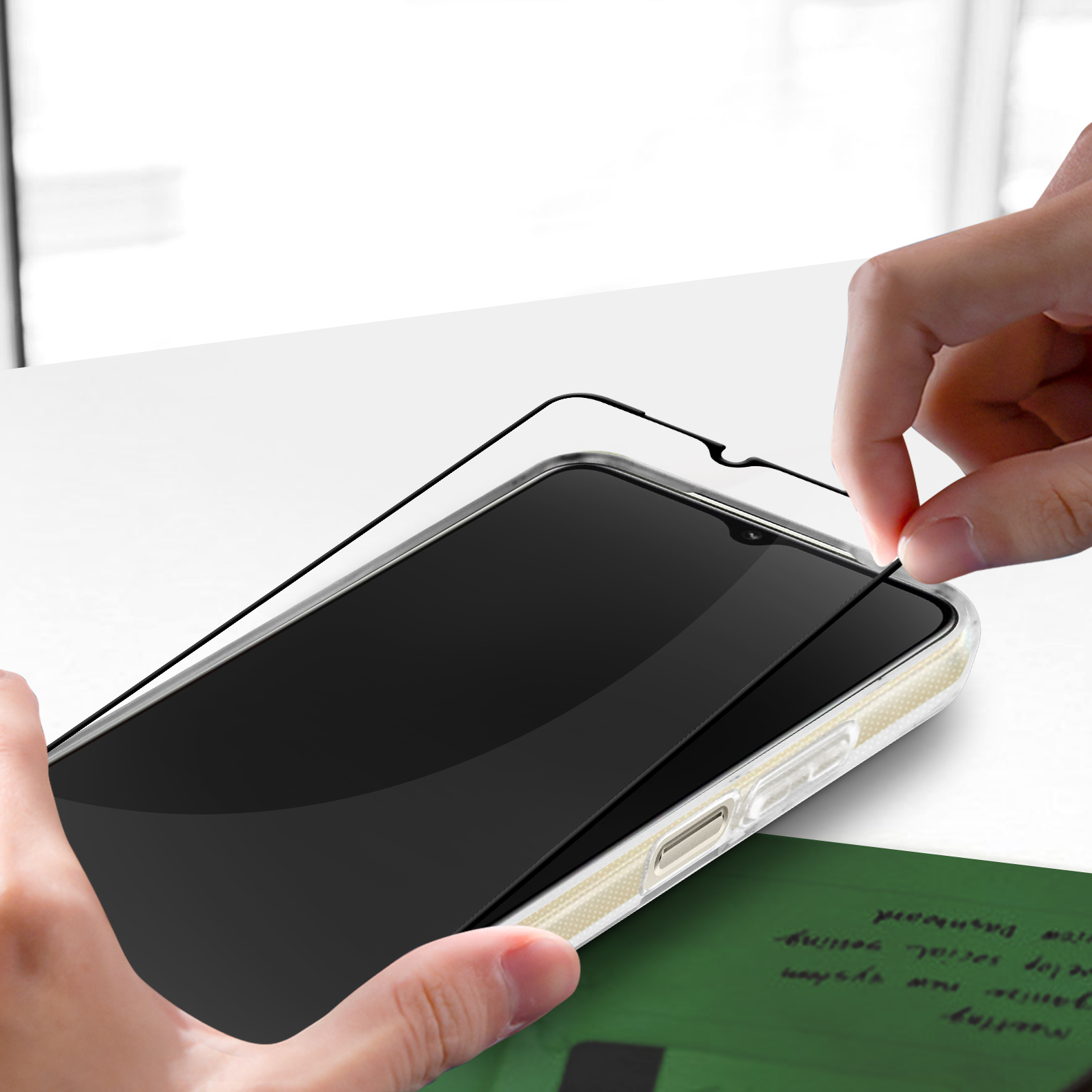 Una mano applica una protezione per lo schermo a un telefono. Un post-it verde è sotto il telefono.