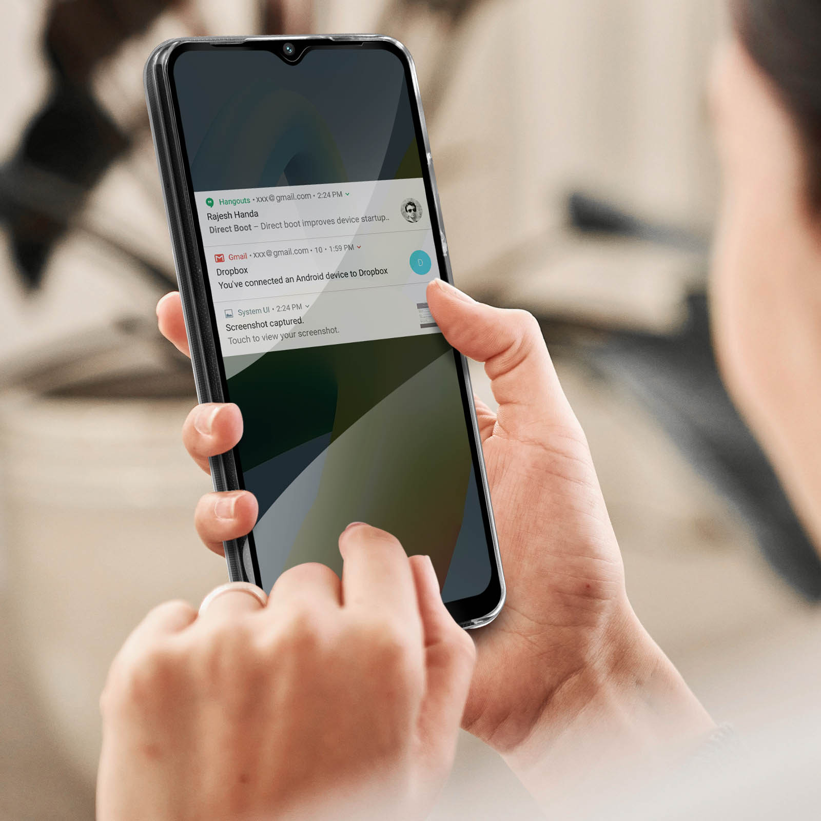 Una mano che tiene un telefono nero che mostra le notifiche. Il telefono è in una custodia trasparente. Lo sfondo è un interno sfocato.