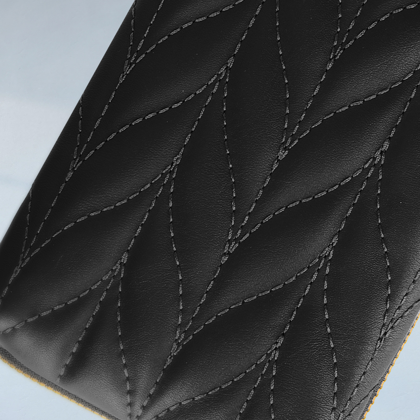 Primo piano di pelle nera con cuciture a diamante. Tessuto giallo visibile sul bordo inferiore.