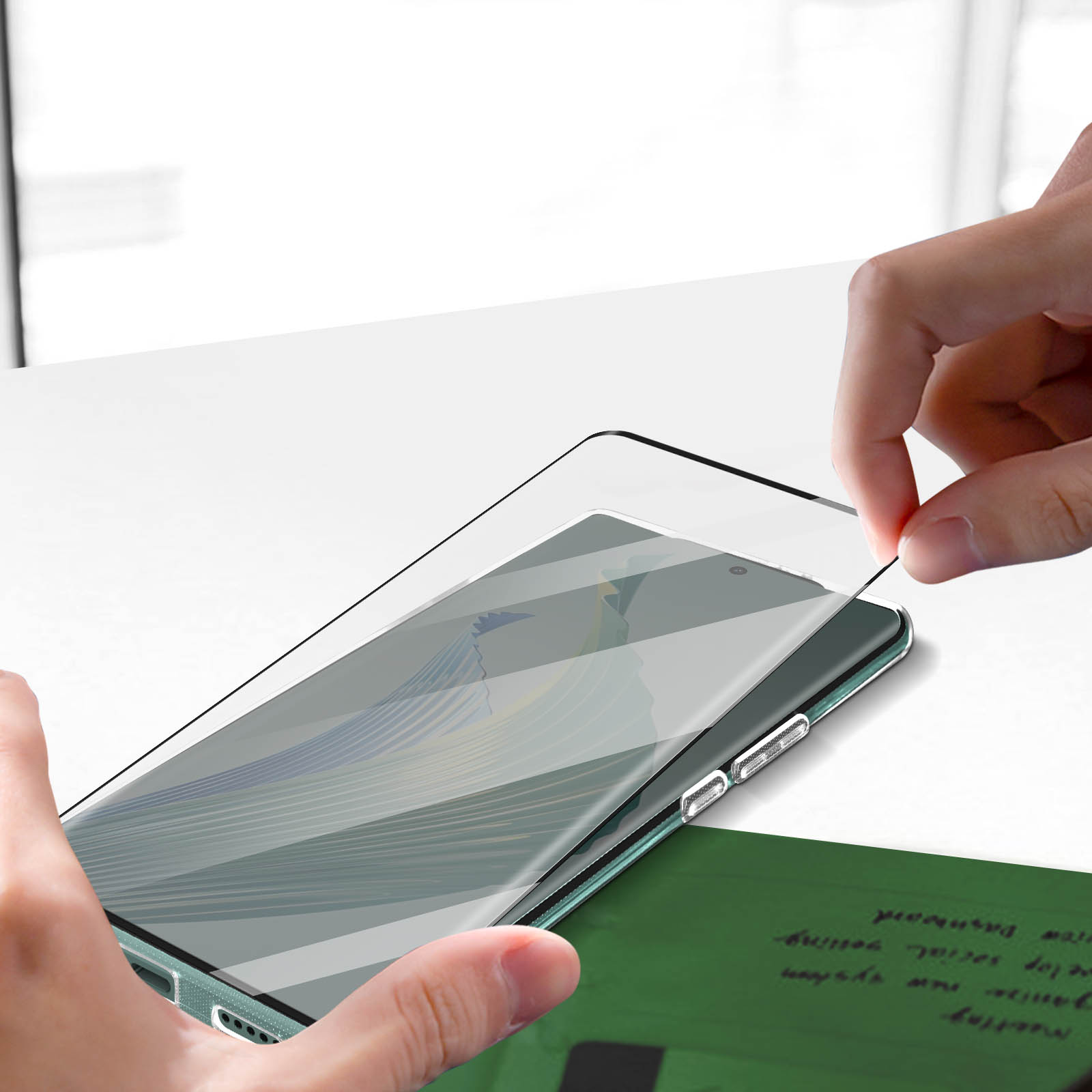 Una mano applica una protezione per lo schermo a un telefono. Sotto c'è un foglio verde con della scrittura.