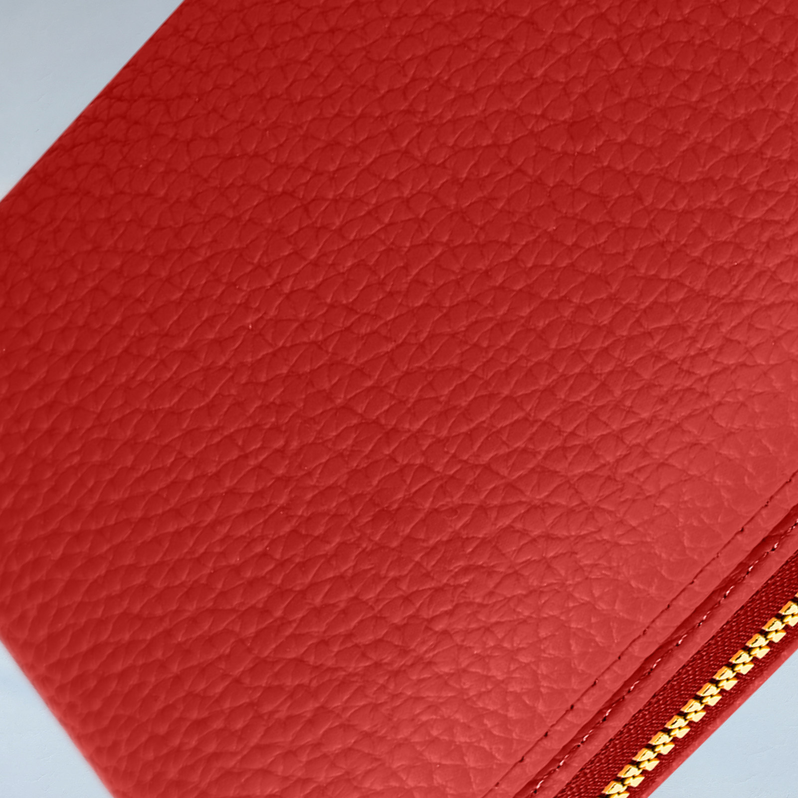 Close-up van een rode, getextureerde lederen portemonnee-telefoonhoes met een gouden rits.