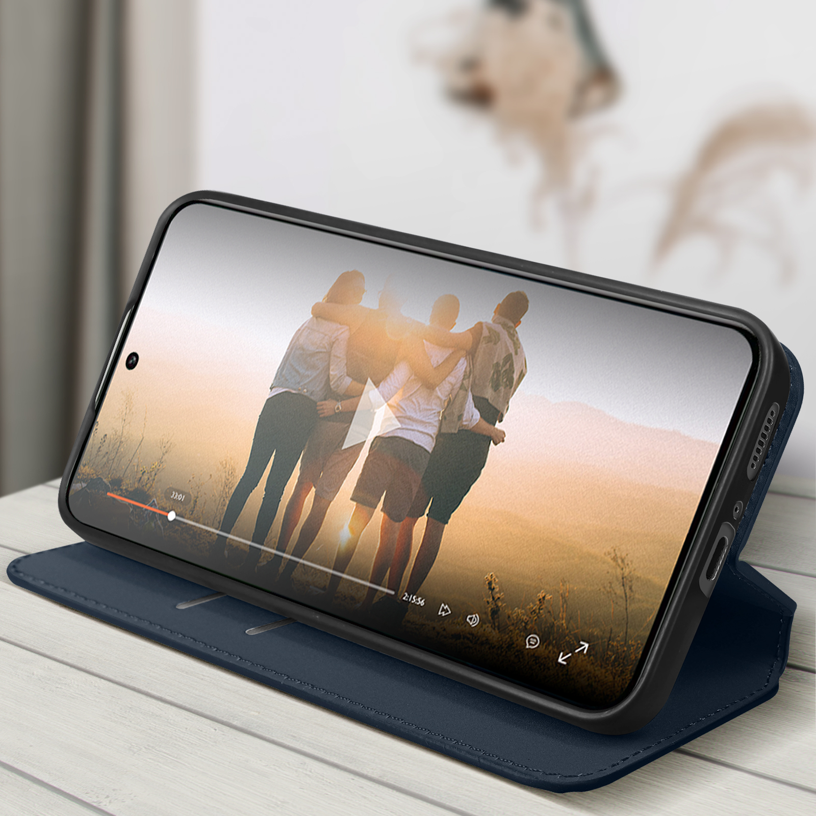 Telefono che riproduce video con persone che si abbracciano, in custodia blu su un tavolo.