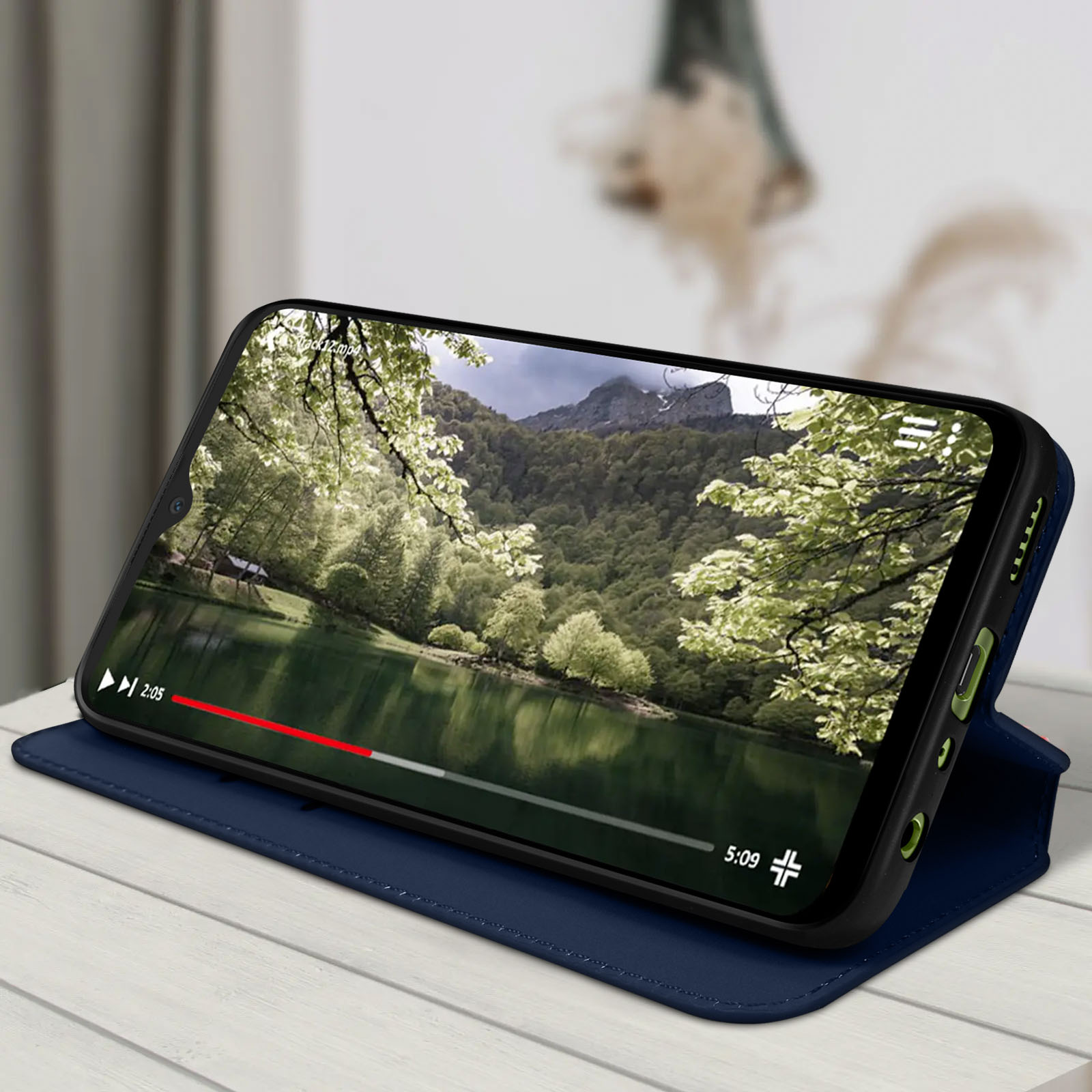 Un téléphone dans un étui bleu affiche une vidéo d'un lac et d'arbres.