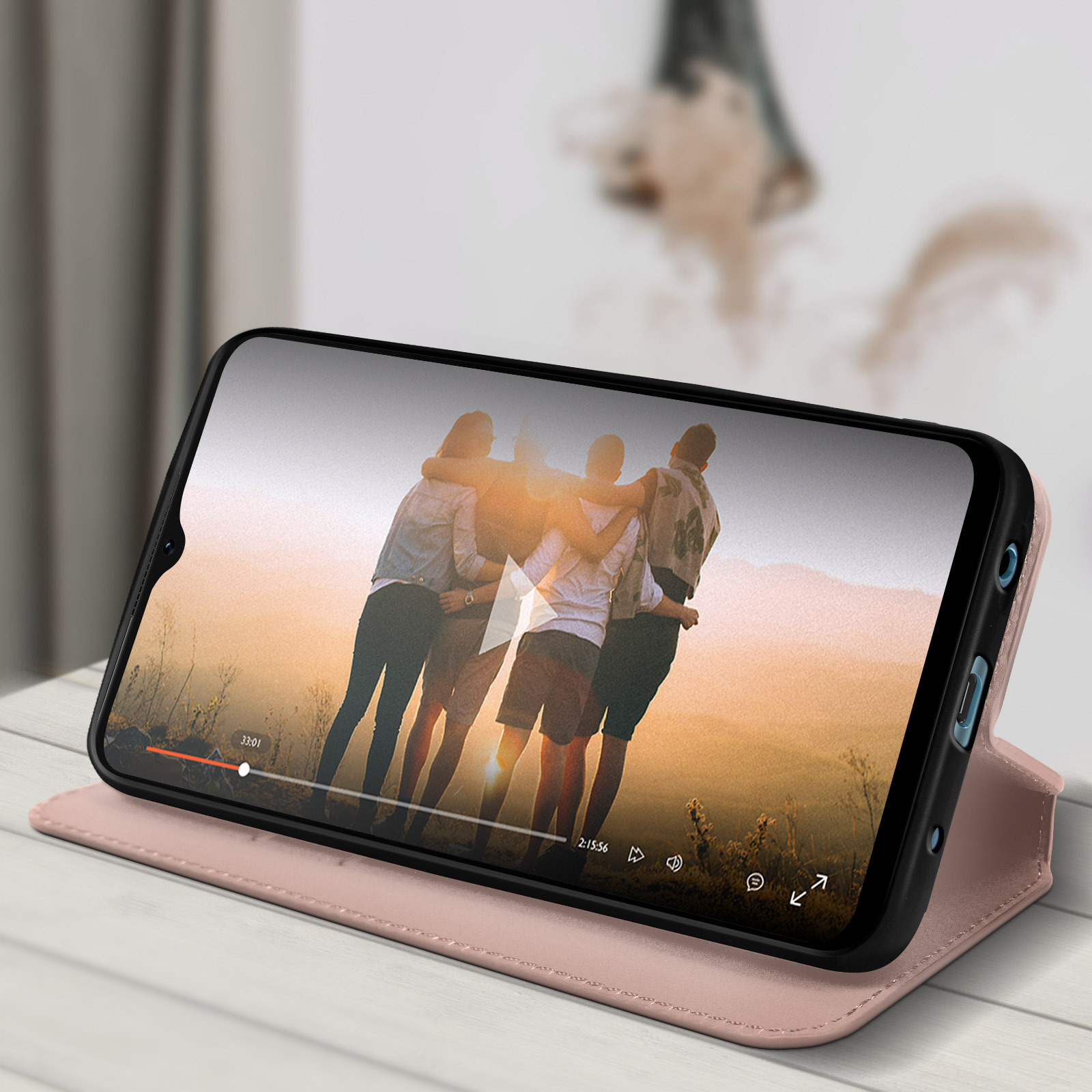Un telefono mostra un video di persone. Poggia su un tavolo con una custodia rosa.
