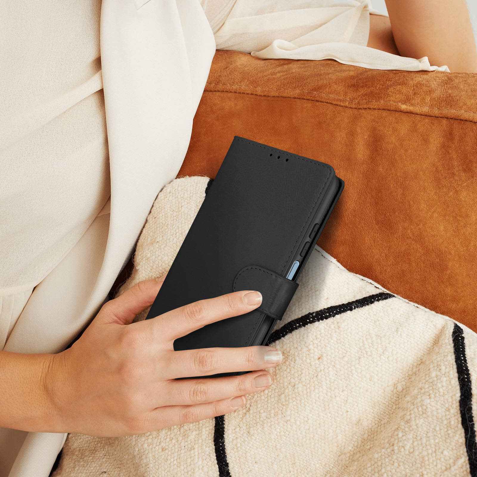 Une personne tenant un étui de téléphone noir. La personne est assise. L'arrière-plan est un oreiller marron et une couverture blanche.