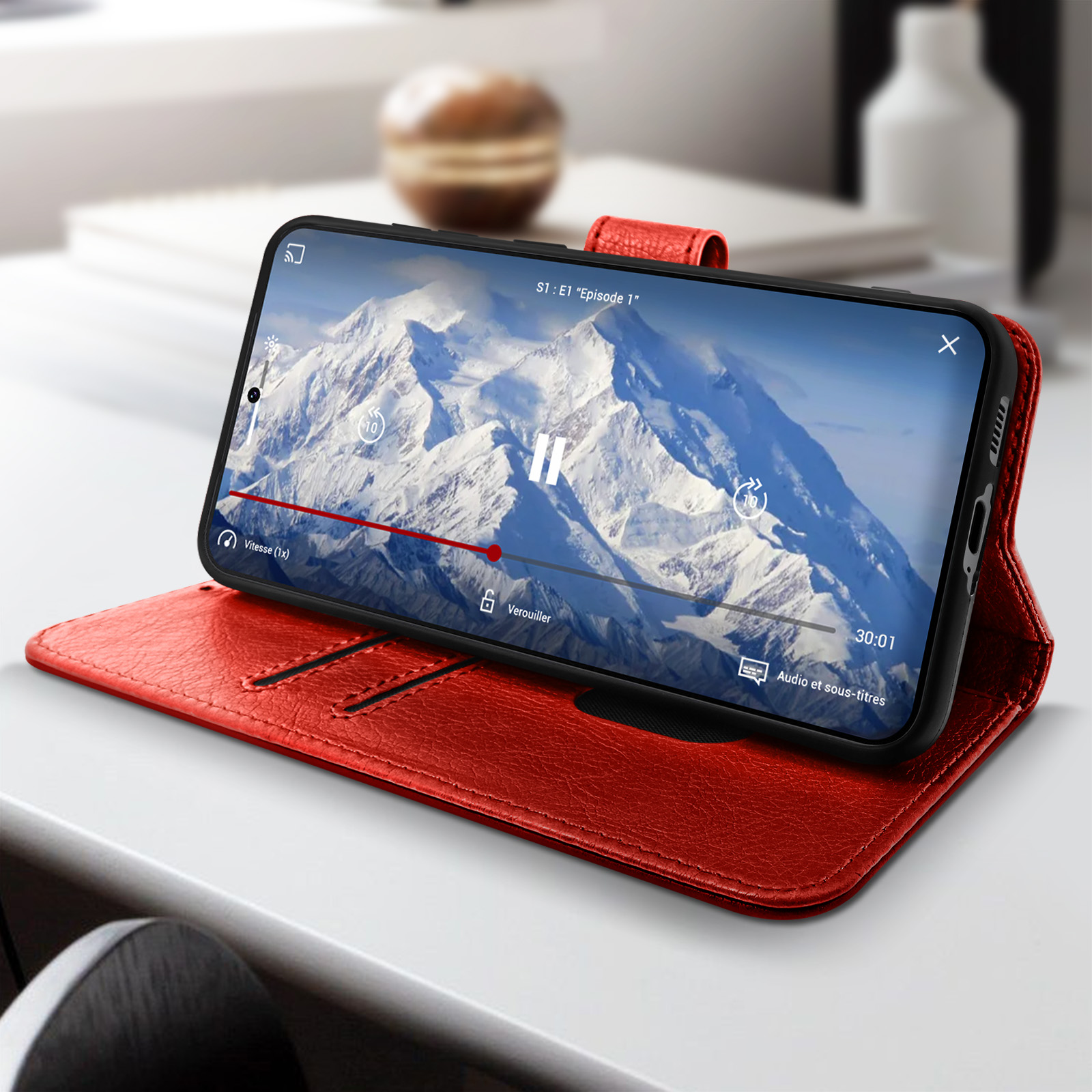 Een telefoon in een rode leren hoes, met een video op het scherm, op een witte tafel.