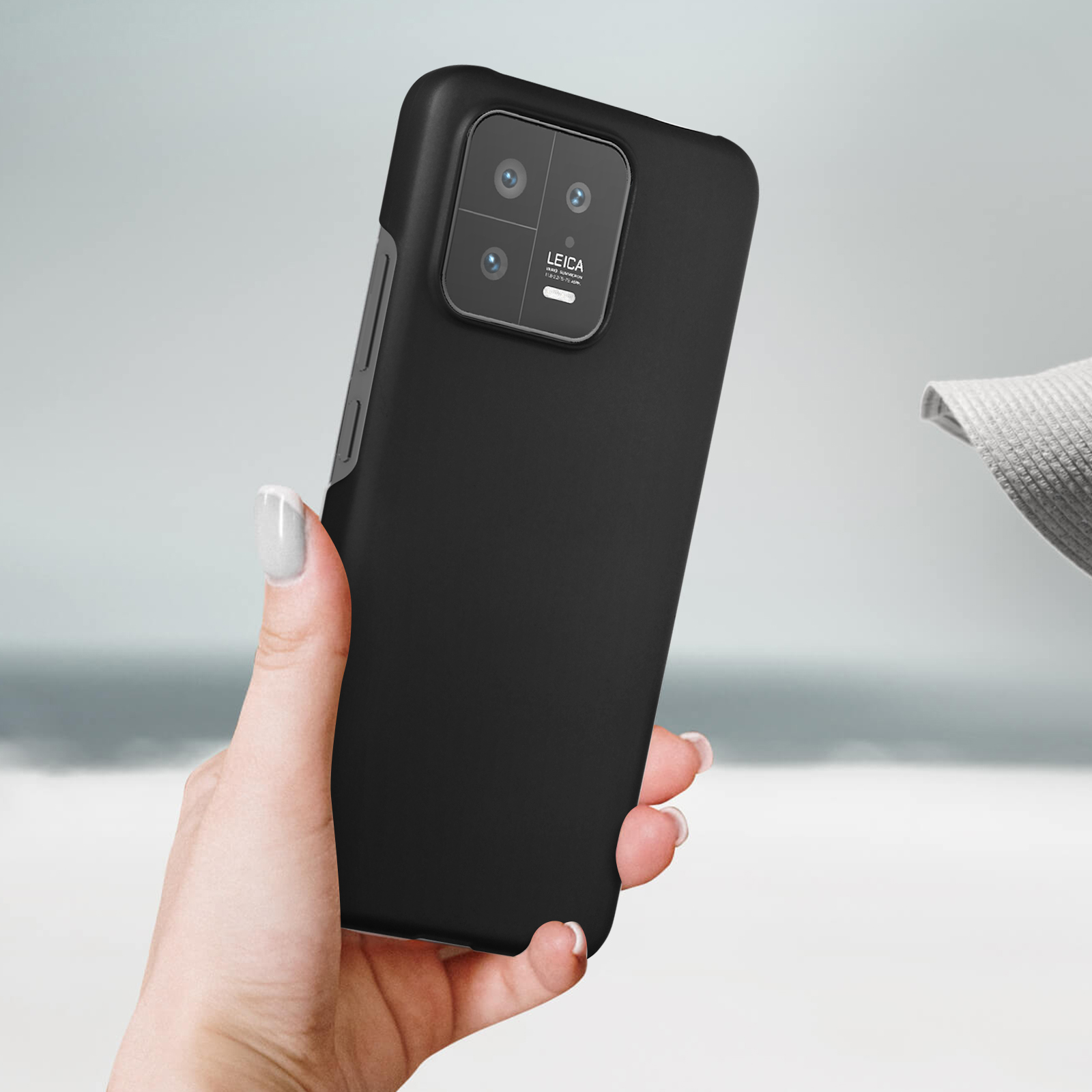 Een persoon houdt een zwarte telefoonhoes vast, met een strandscène op de achtergrond.