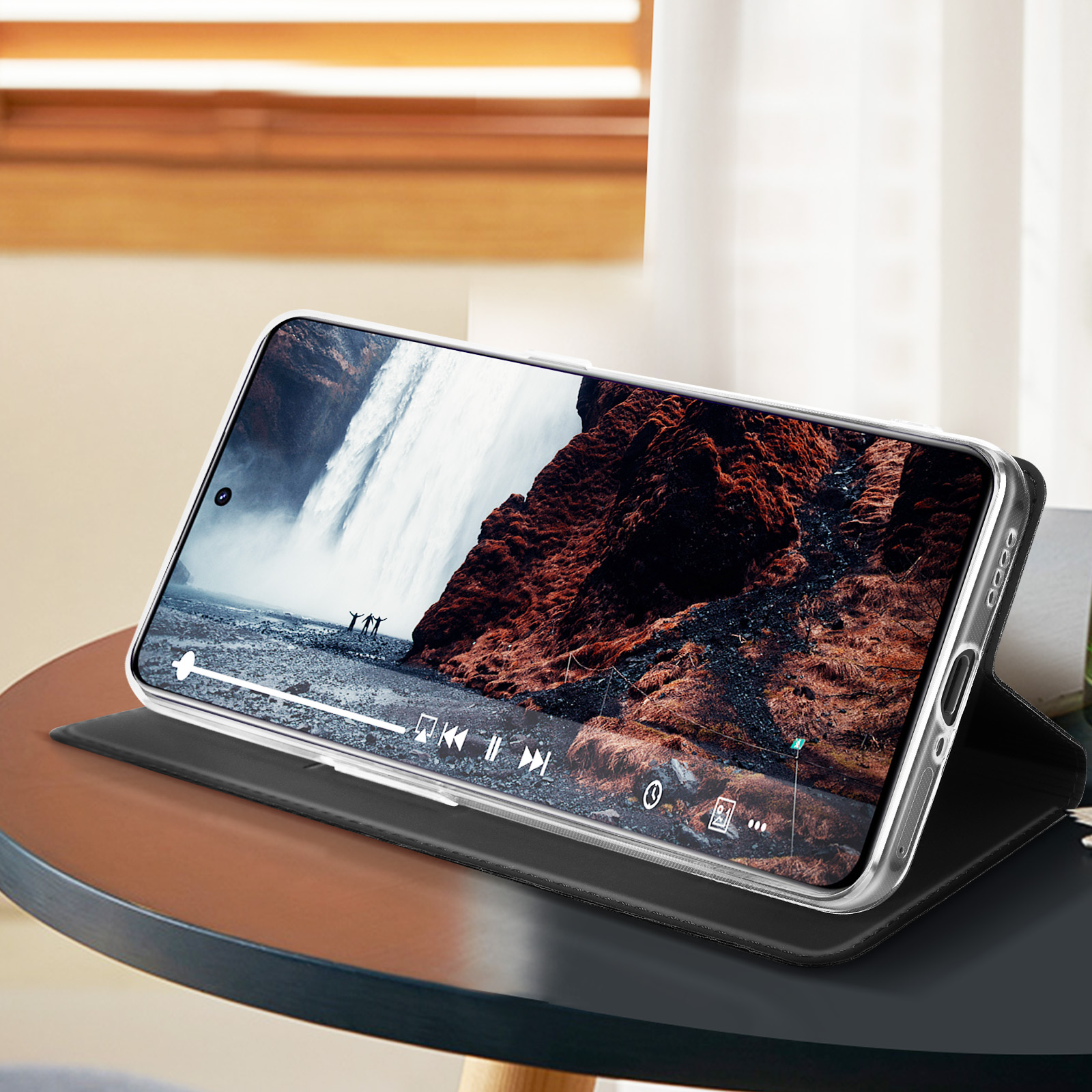 Telefono in una custodia, che mostra un video di cascata, appoggiato su un tavolo con una finestra sullo sfondo.