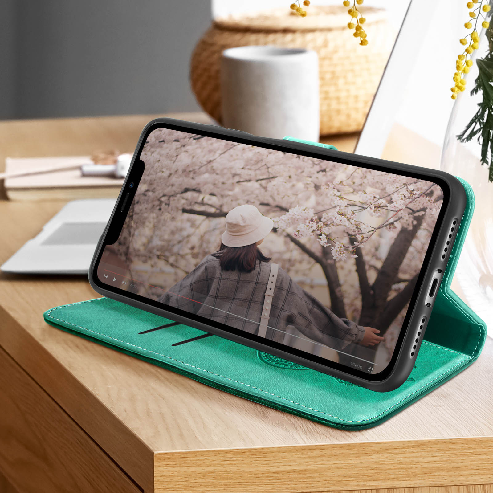 Telefono in una custodia di pelle verde che mostra un video di una donna. La custodia è su un tavolo di legno.