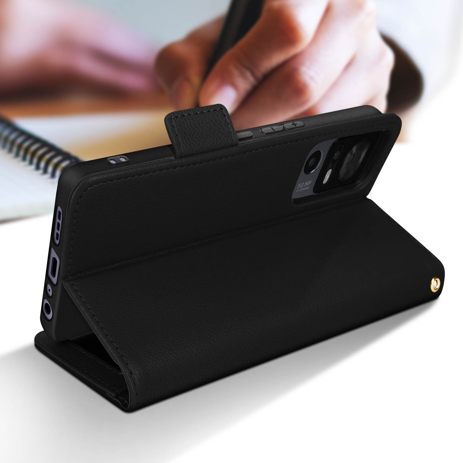 Main d'une personne écrivant sur un cahier. Un téléphone est dans un étui en cuir noir.