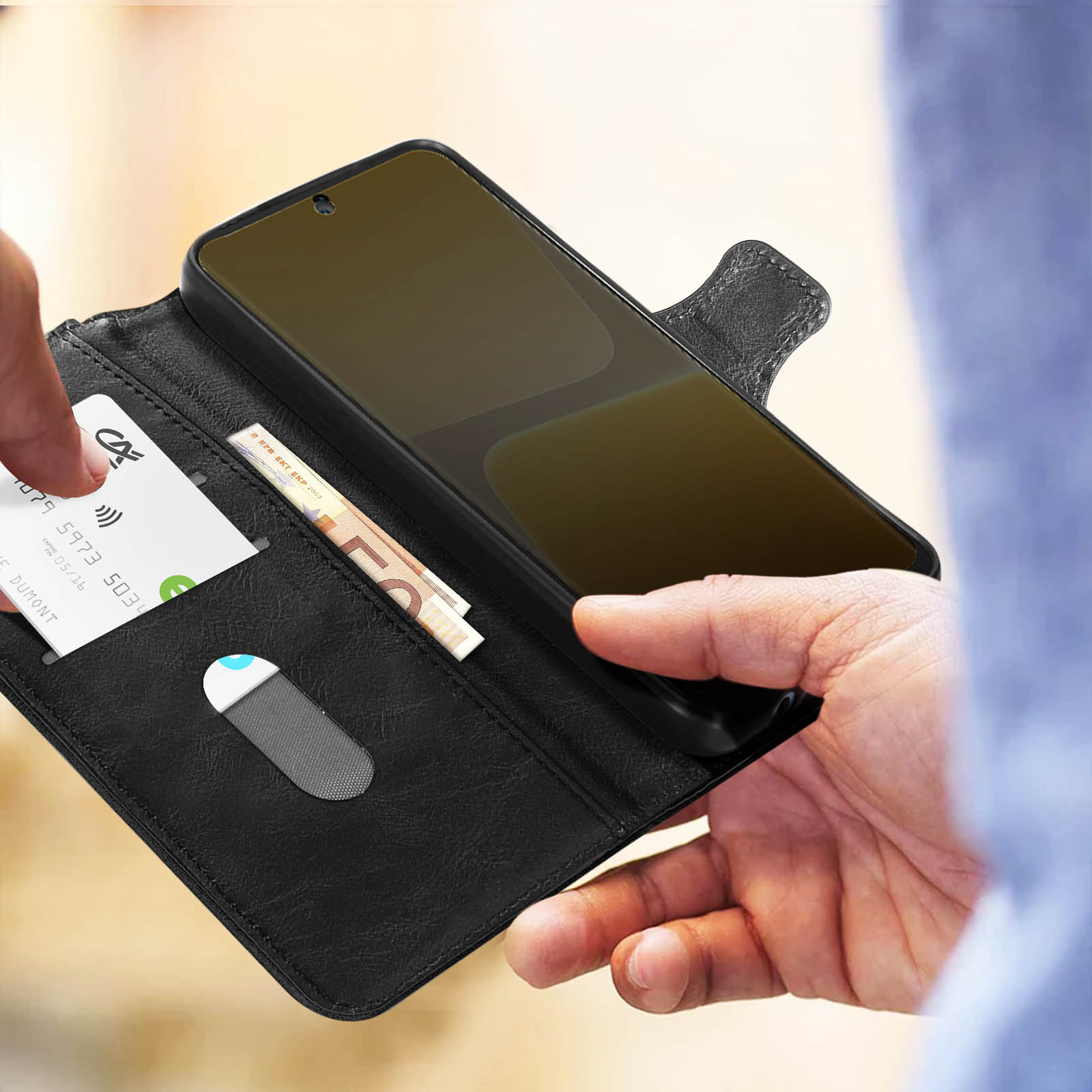 Mano che tiene una custodia nera per telefono, una carta e un po' di contanti. Il telefono è dentro.