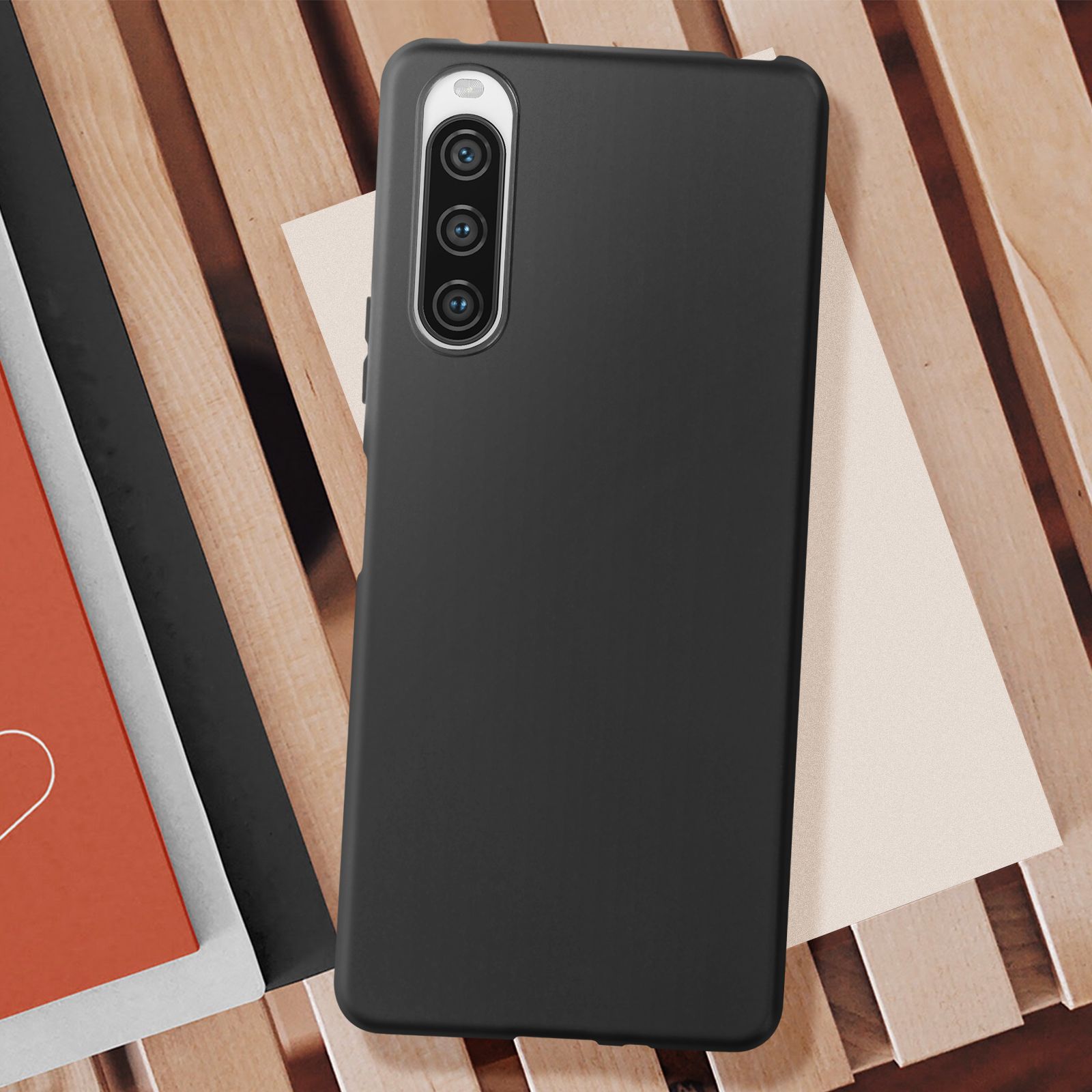 Telefono nero su una superficie di legno, con un libro rosso e carta color crema nelle vicinanze. Il telefono è in una custodia.