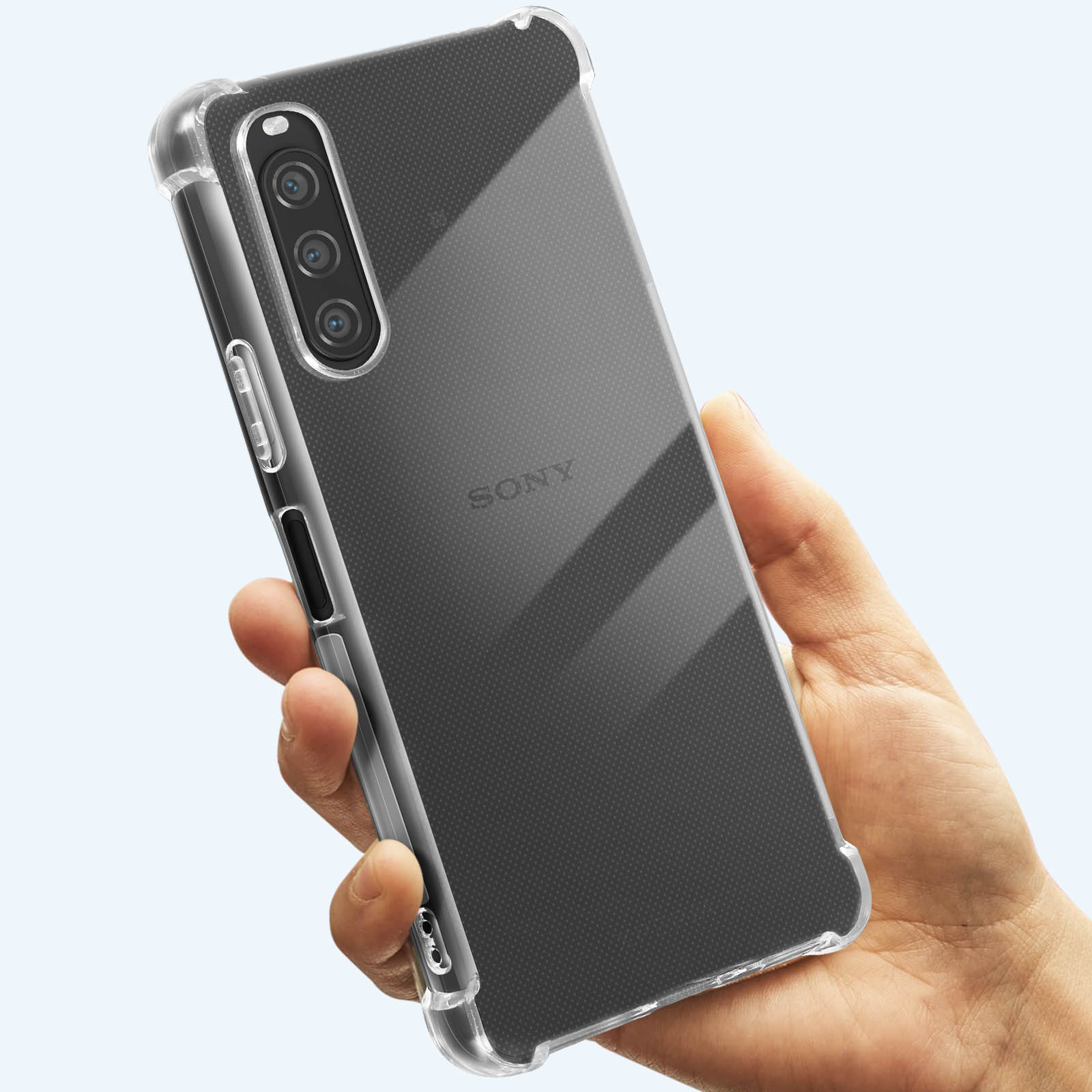Una mano tiene un telefono in una custodia trasparente. Il telefono ha una tripla fotocamera. Lo sfondo è una superficie sfumata azzurra.
