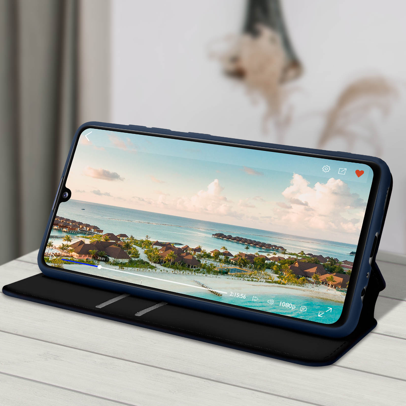 Un teléfono en una funda azul oscuro está abierto, mostrando un video con una escena de playa en el fondo.