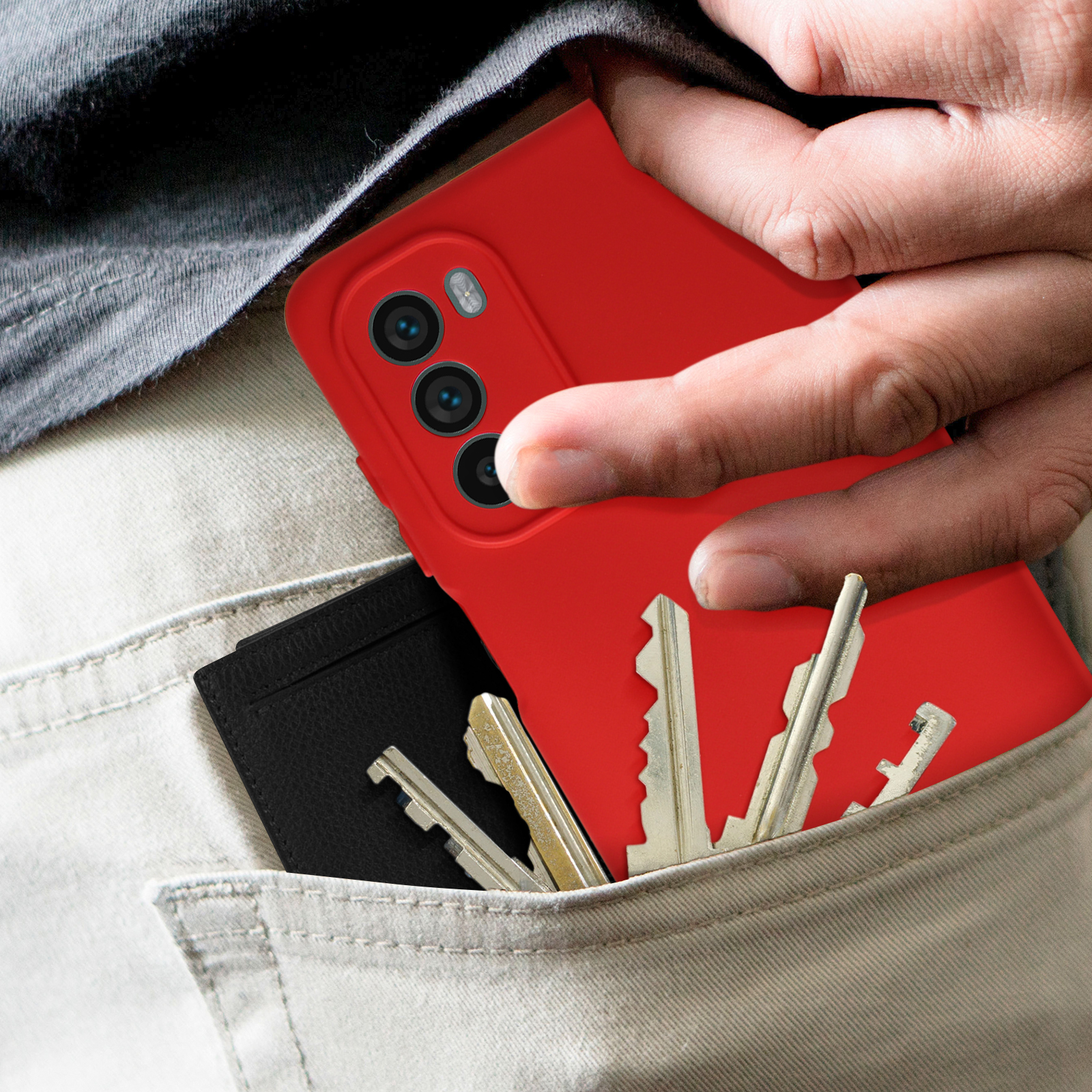 Una custodia rossa per telefono è in una tasca con chiavi e un porta carte nero. Una mano tiene il telefono.