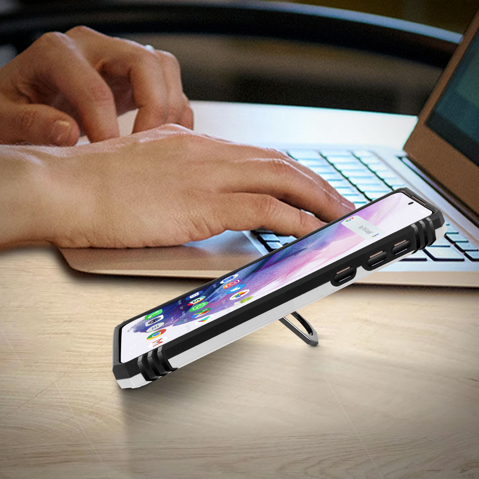 Een persoon typt op een laptop. Een telefoon staat op de voorgrond.
