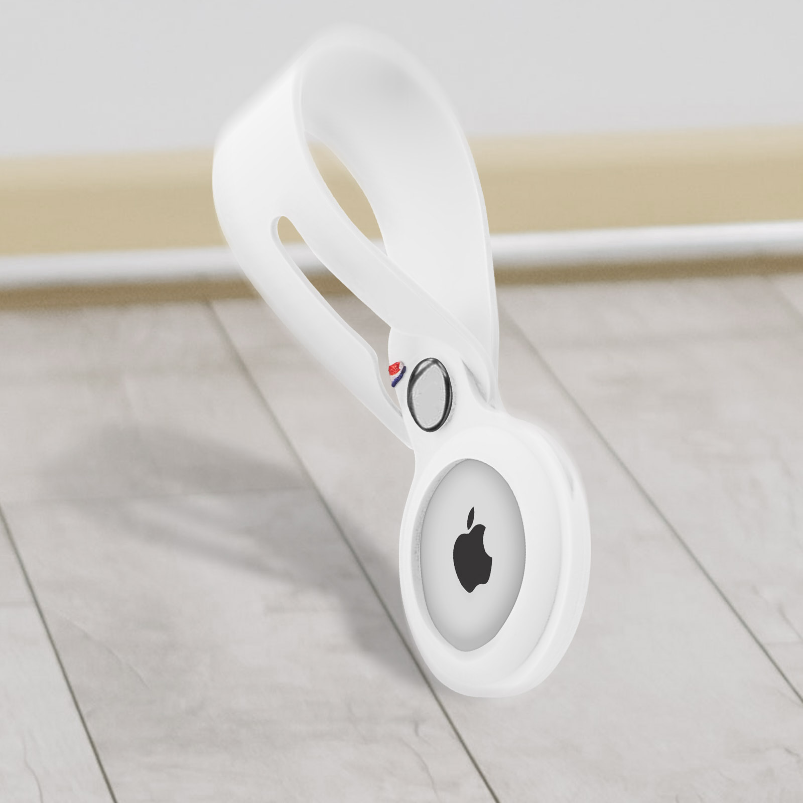 Apple AirTag bianco in un supporto bianco. Il supporto ha un anello, ed è su una superficie di legno.
