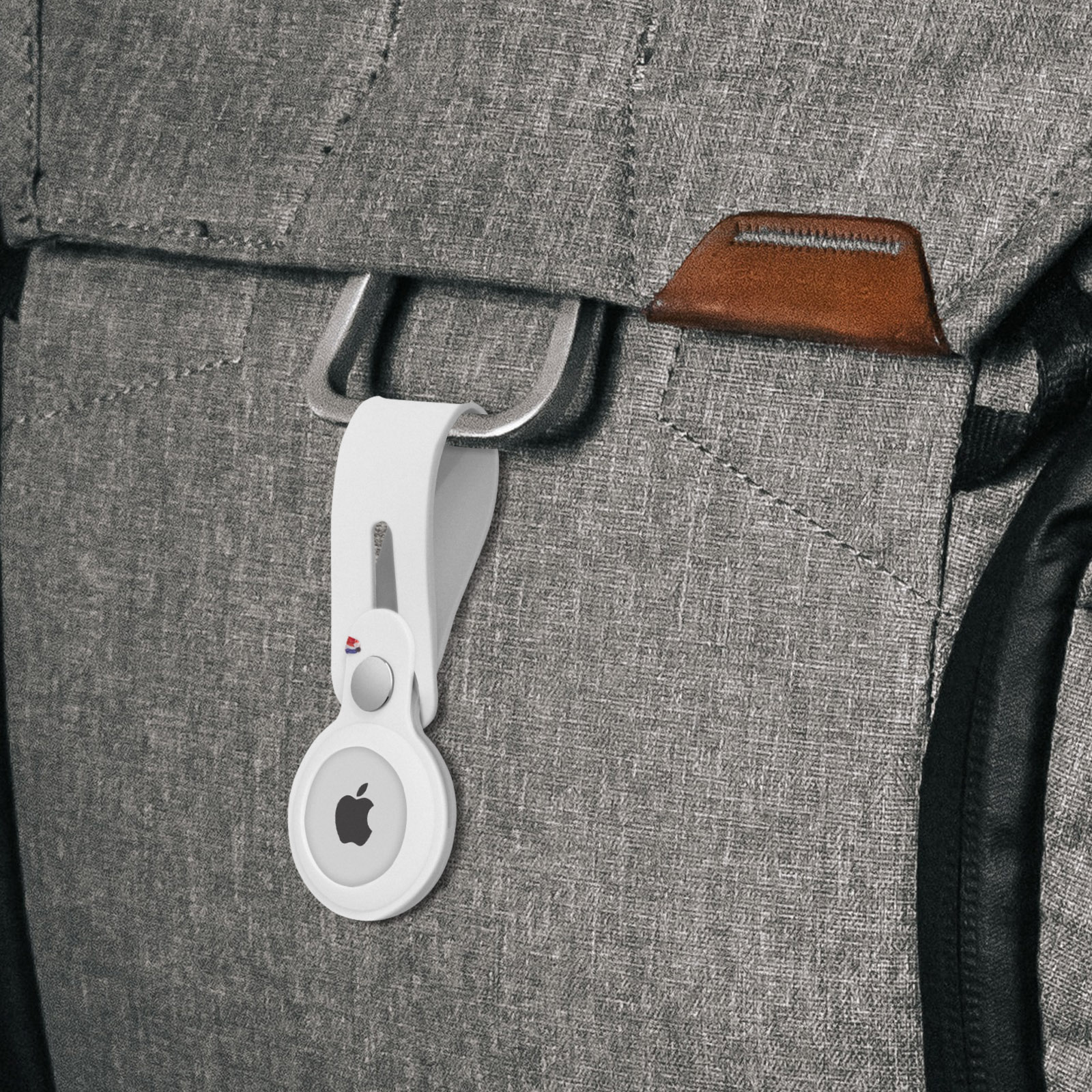 Un Apple AirTag bianco attaccato a uno zaino grigio. Dettagli in pelle marrone.