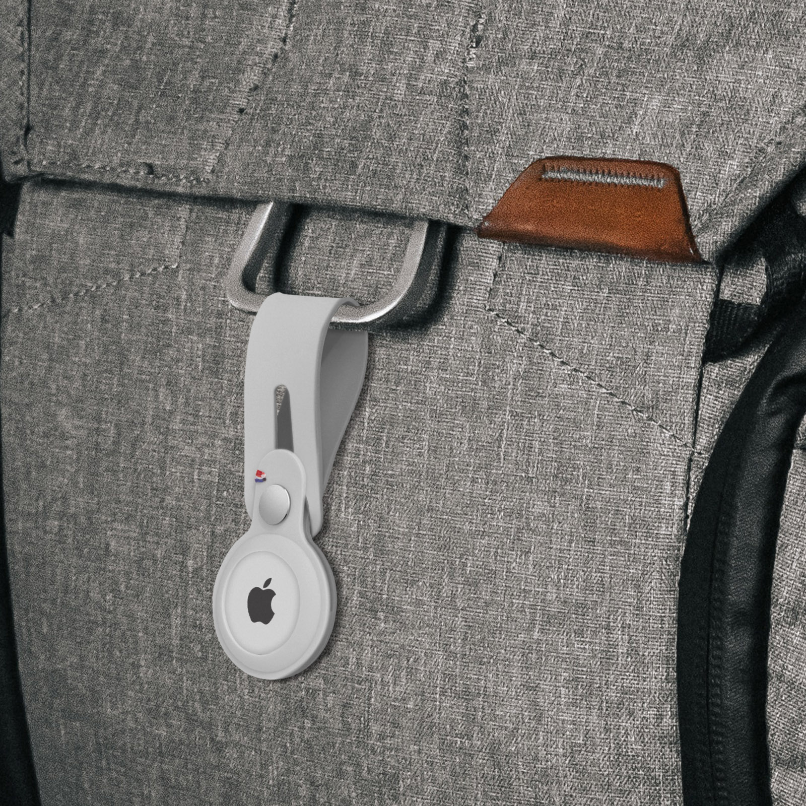 Un Apple AirTag bianco attaccato a una cinghia di uno zaino grigio.