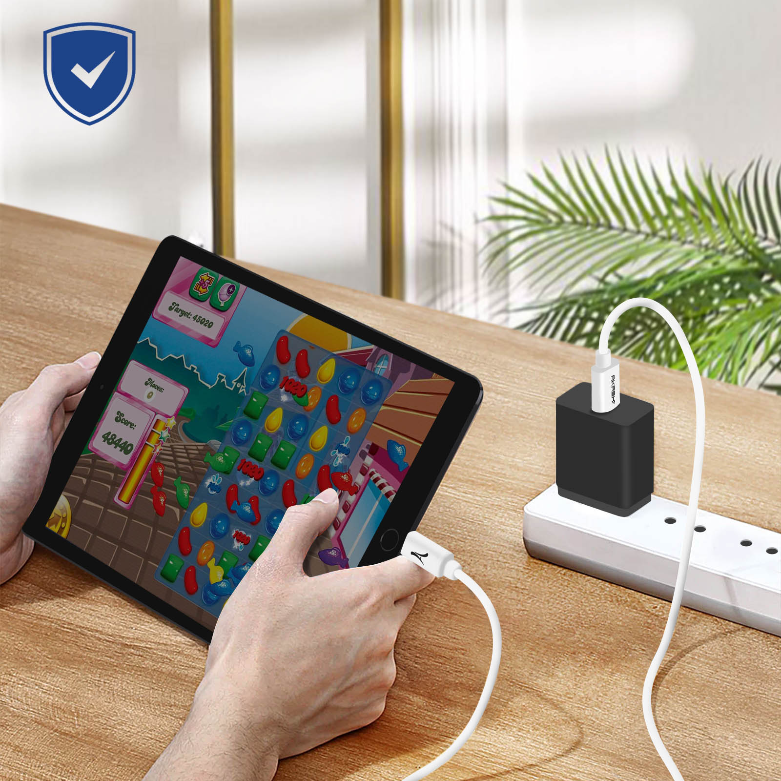 Una persona sosteniendo una tableta jugando un juego, conectado a un cargador en una mesa.