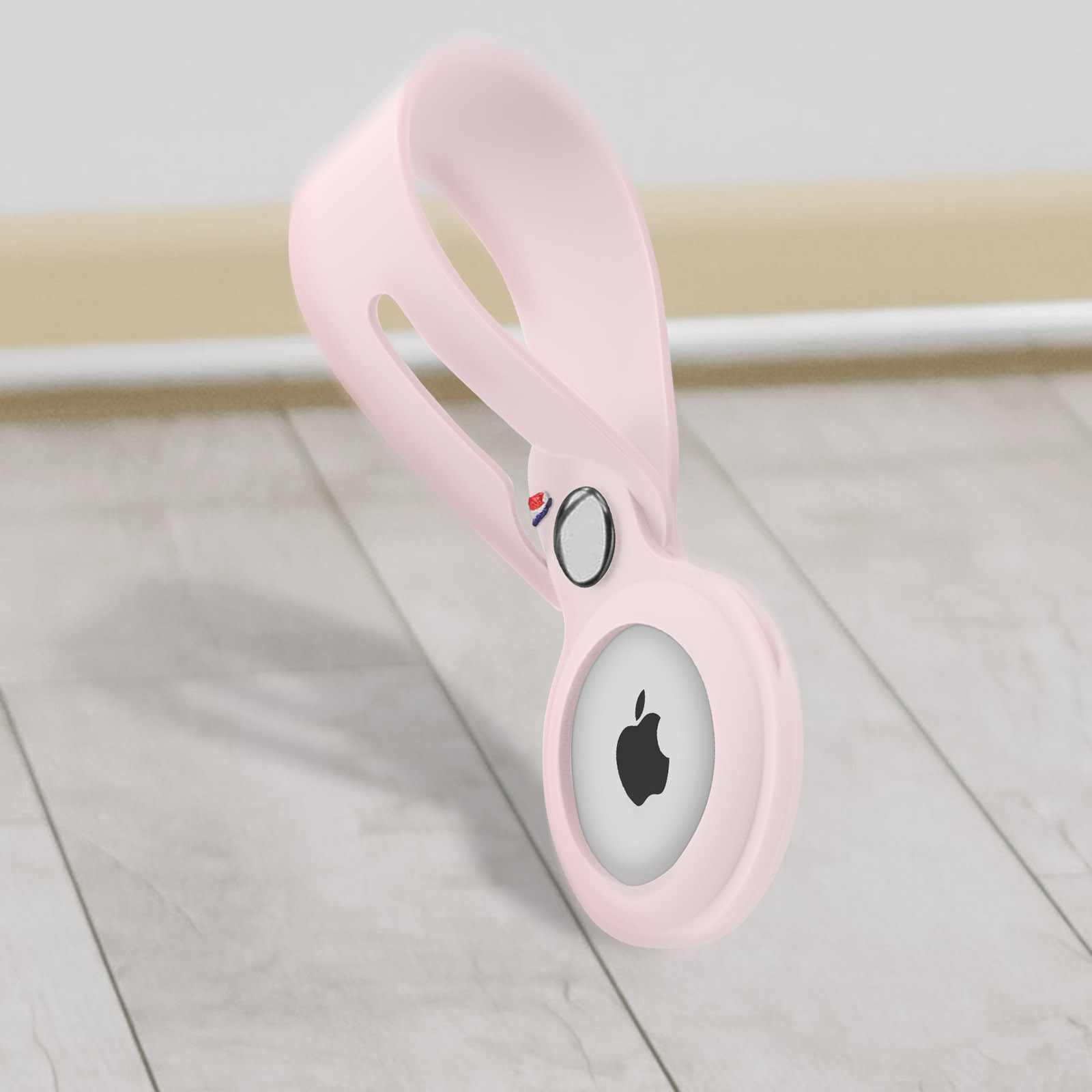 Rosa Apple AirTag Hülle. Sie hängt über einem hellen Holzboden.