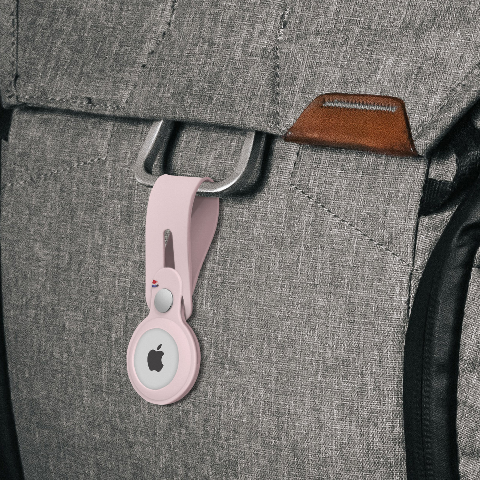 Rosa AirTag-Halterung an grauem Rucksack befestigt. Apple-Logo sichtbar.