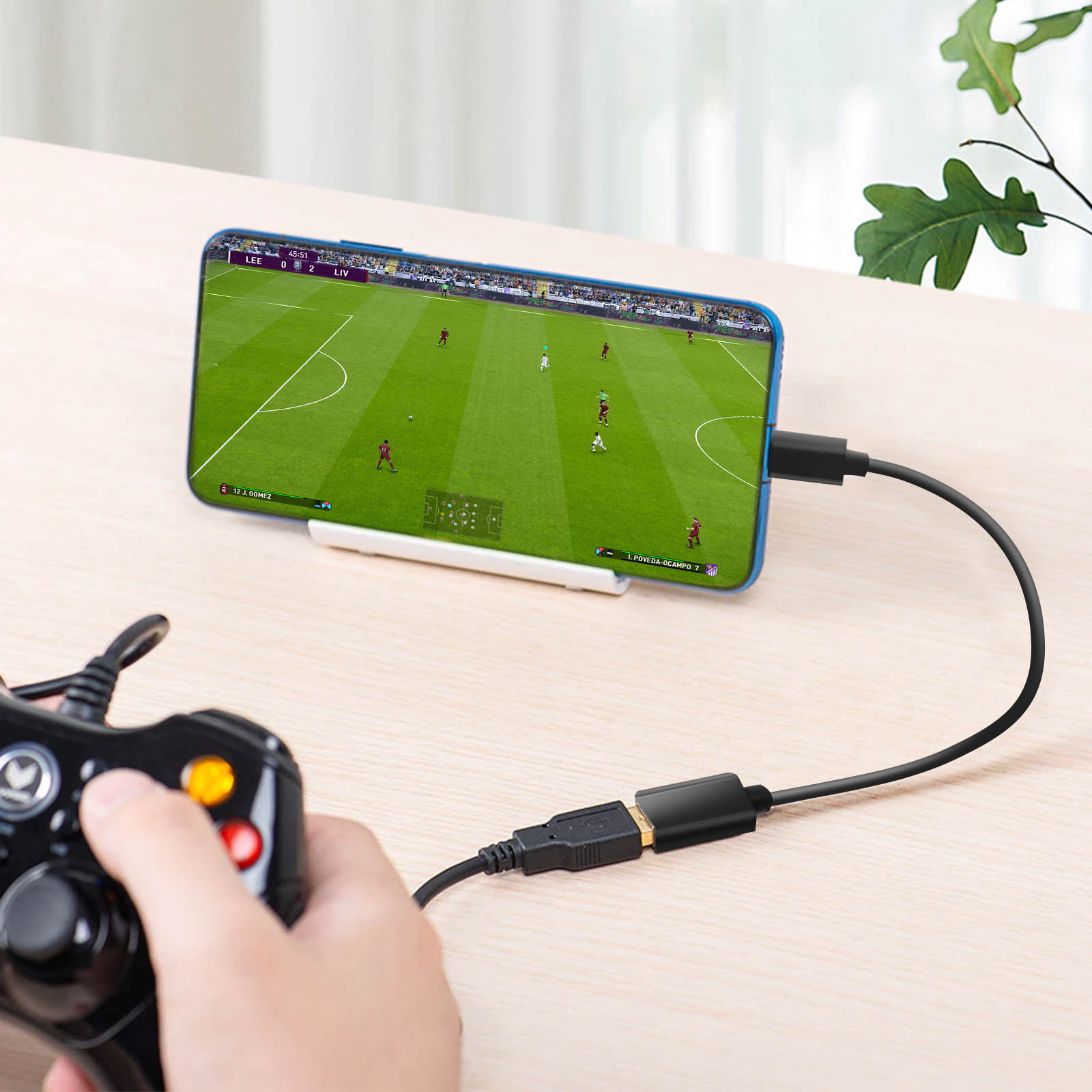 Telefono collegato a un controller che gioca a calcio. Cavo nero visibile.