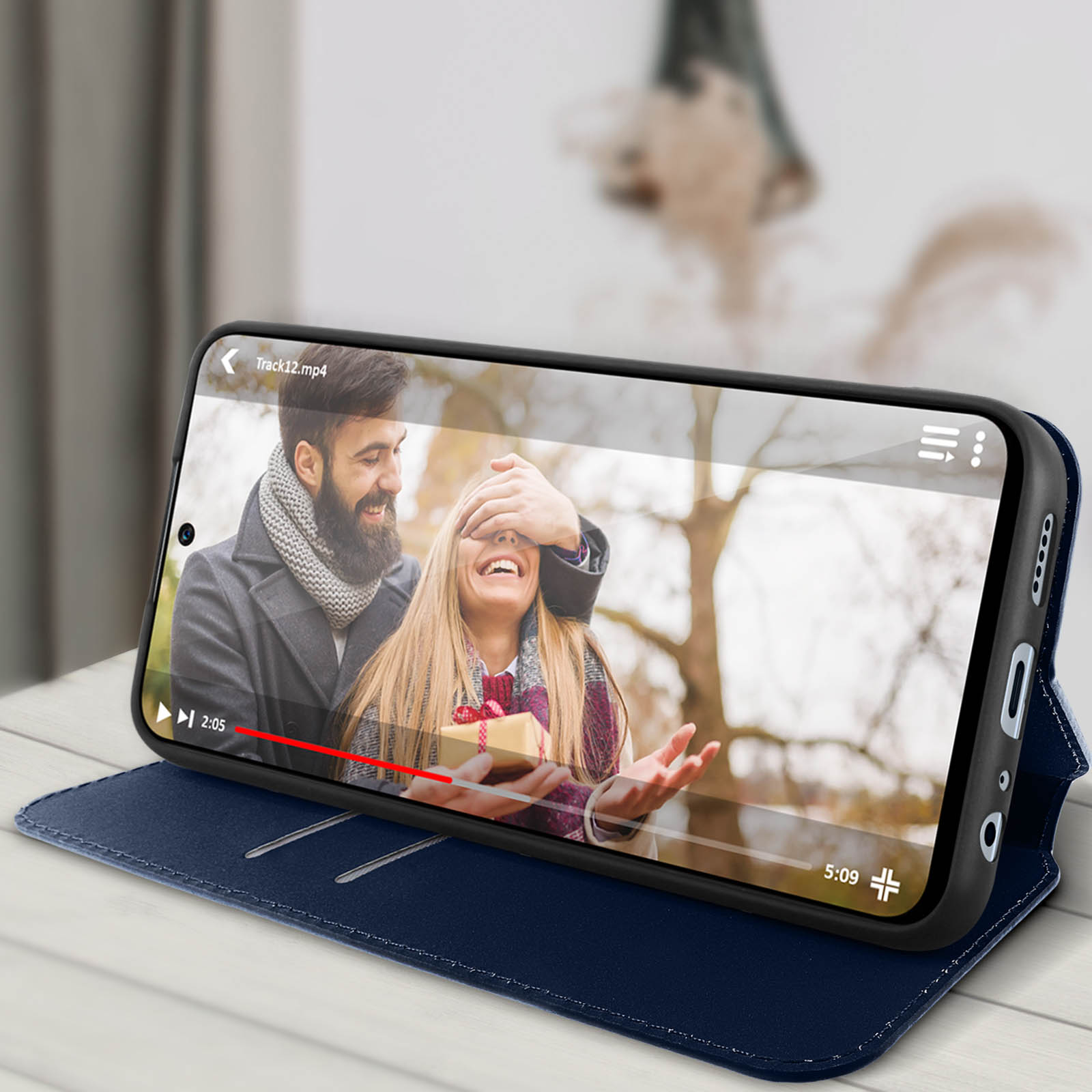 Téléphone dans un étui bleu affichant une vidéo d'un couple. Le téléphone est sur une table, avec un arrière-plan flou.