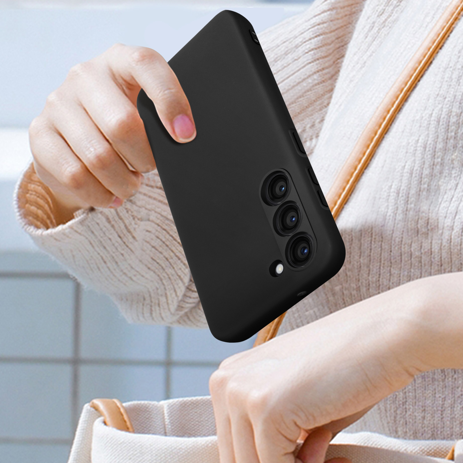 Een persoon houdt een zwarte telefoonhoes vast, met de cameralenzen zichtbaar. De telefoon is zwart.