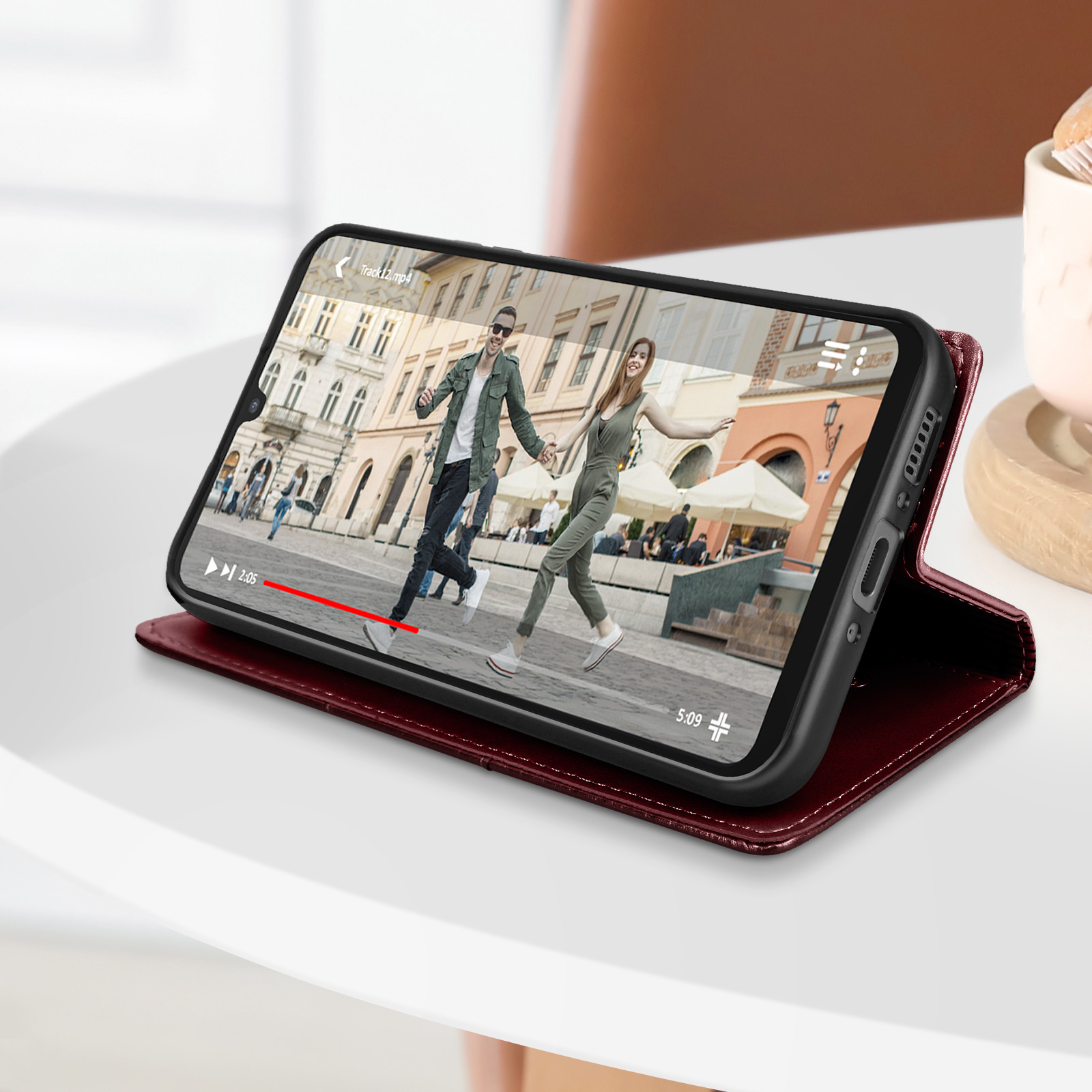 Een telefoon toont een video. De telefoon zit in een rode hoes, rustend op een tafel. Een stel loopt in de video.