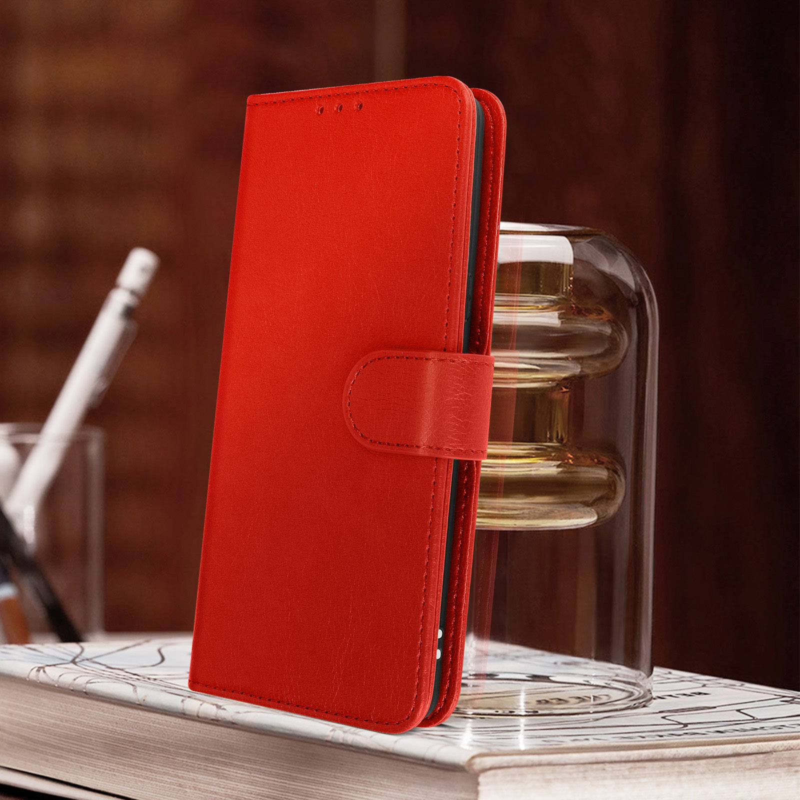 Rote Leder-Handyhülle, geschlossen, auf einem Bücherstapel, mit einem Glas im Hintergrund.