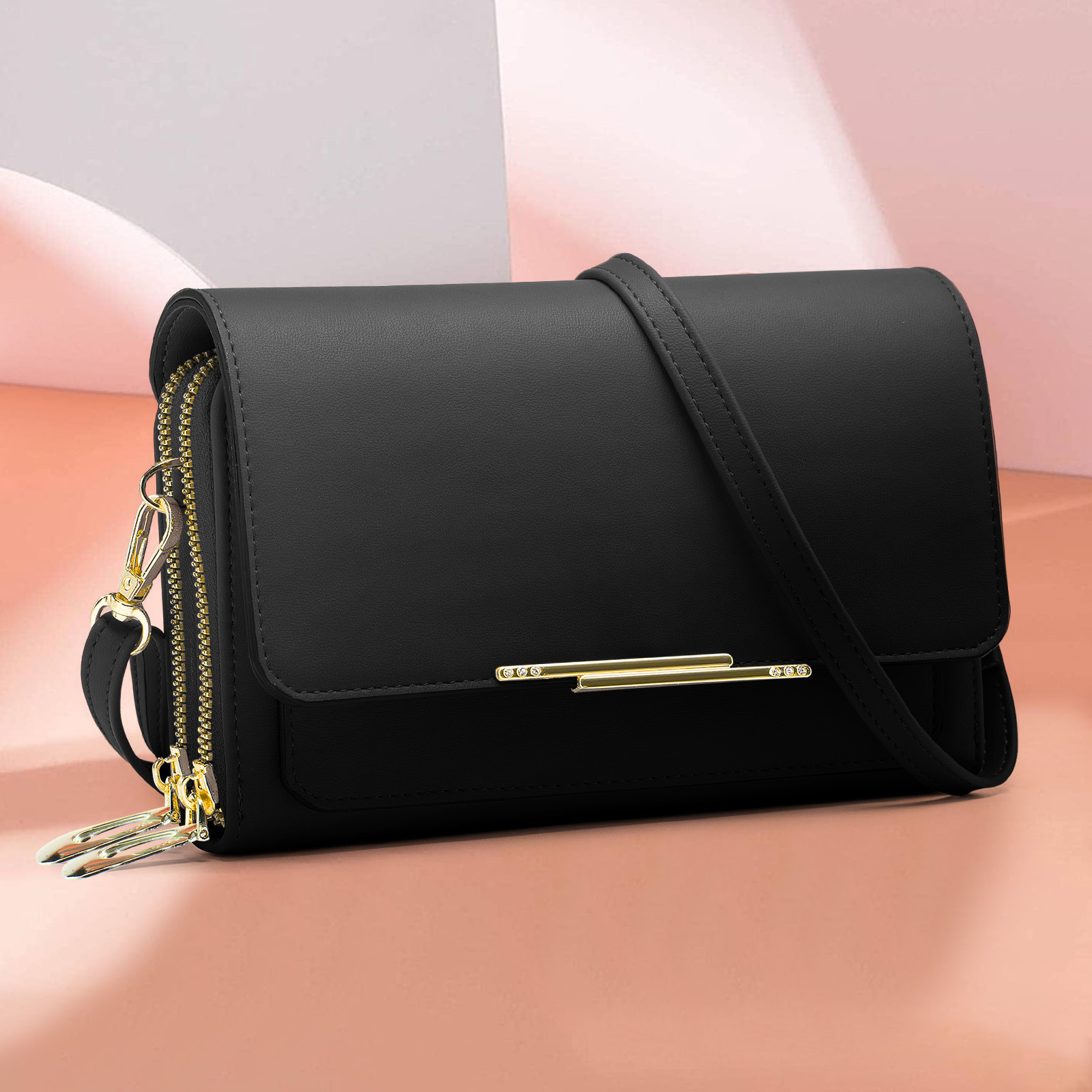 Eine schwarze Geldbörse mit goldenem Reißverschluss und Riemen auf rosa Oberfläche. Vorne ein goldener Balken.