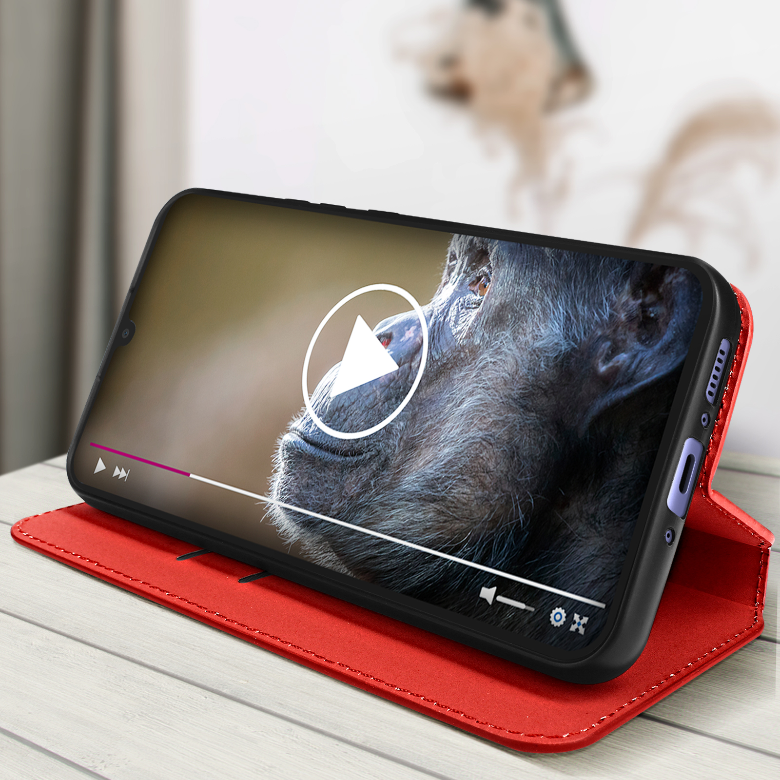 Una custodia rossa per telefono con un telefono che riproduce un video di uno scimpanzé con un pulsante di riproduzione sullo schermo.