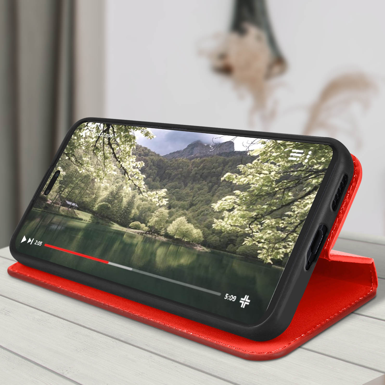 Telefono che mostra video di scena del lago, dentro custodia rossa, su tavolo legno.