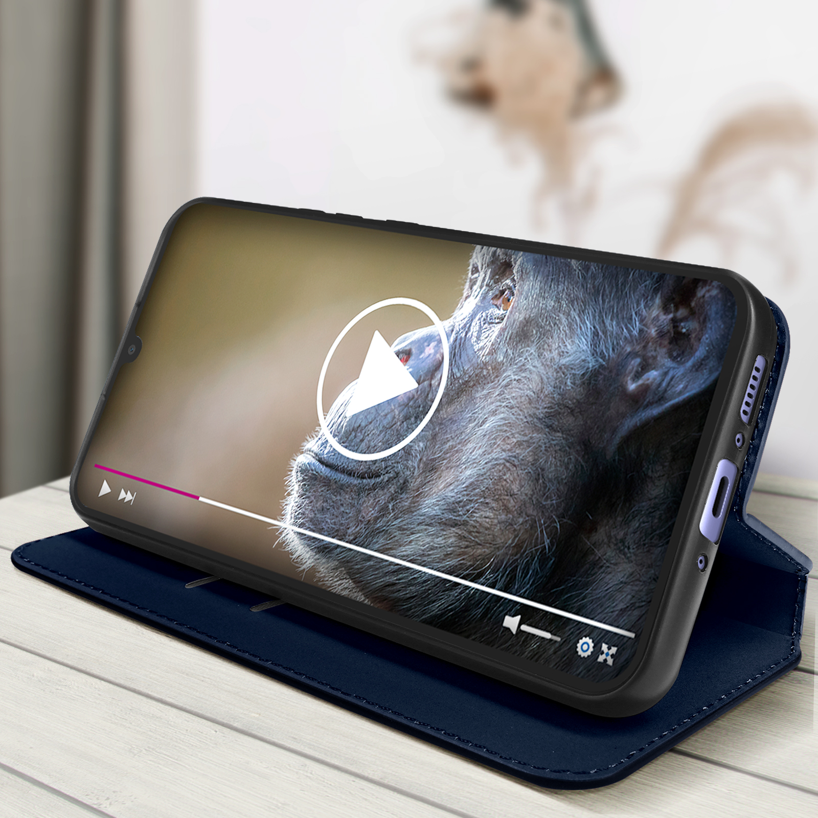 Telefono che mostra un video. Telefono in una custodia blu su una superficie in legno. Sfondo sfocato.