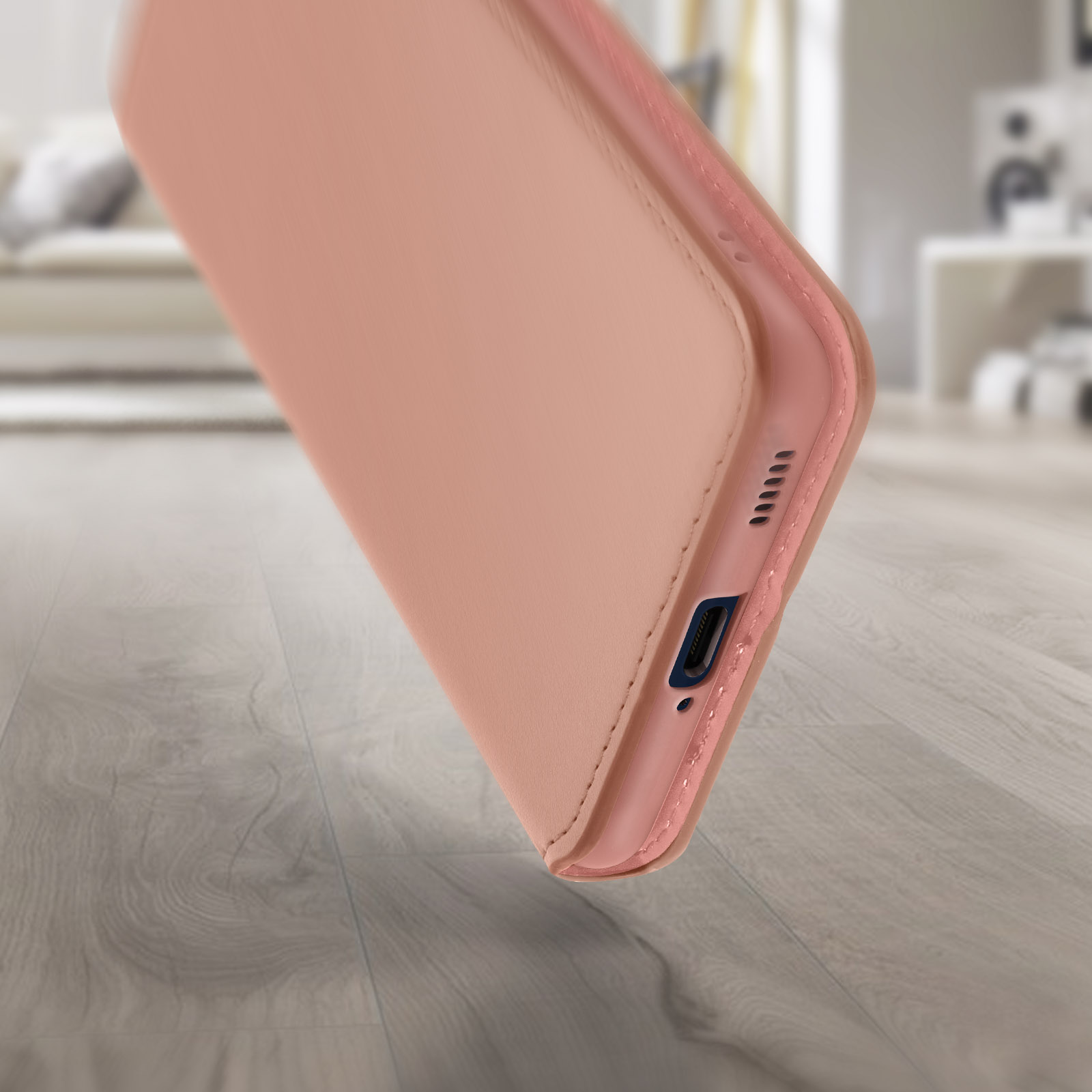 Gros plan sur une coque de téléphone rose clair. Un plancher en bois est au premier plan. Un canapé est en arrière-plan.