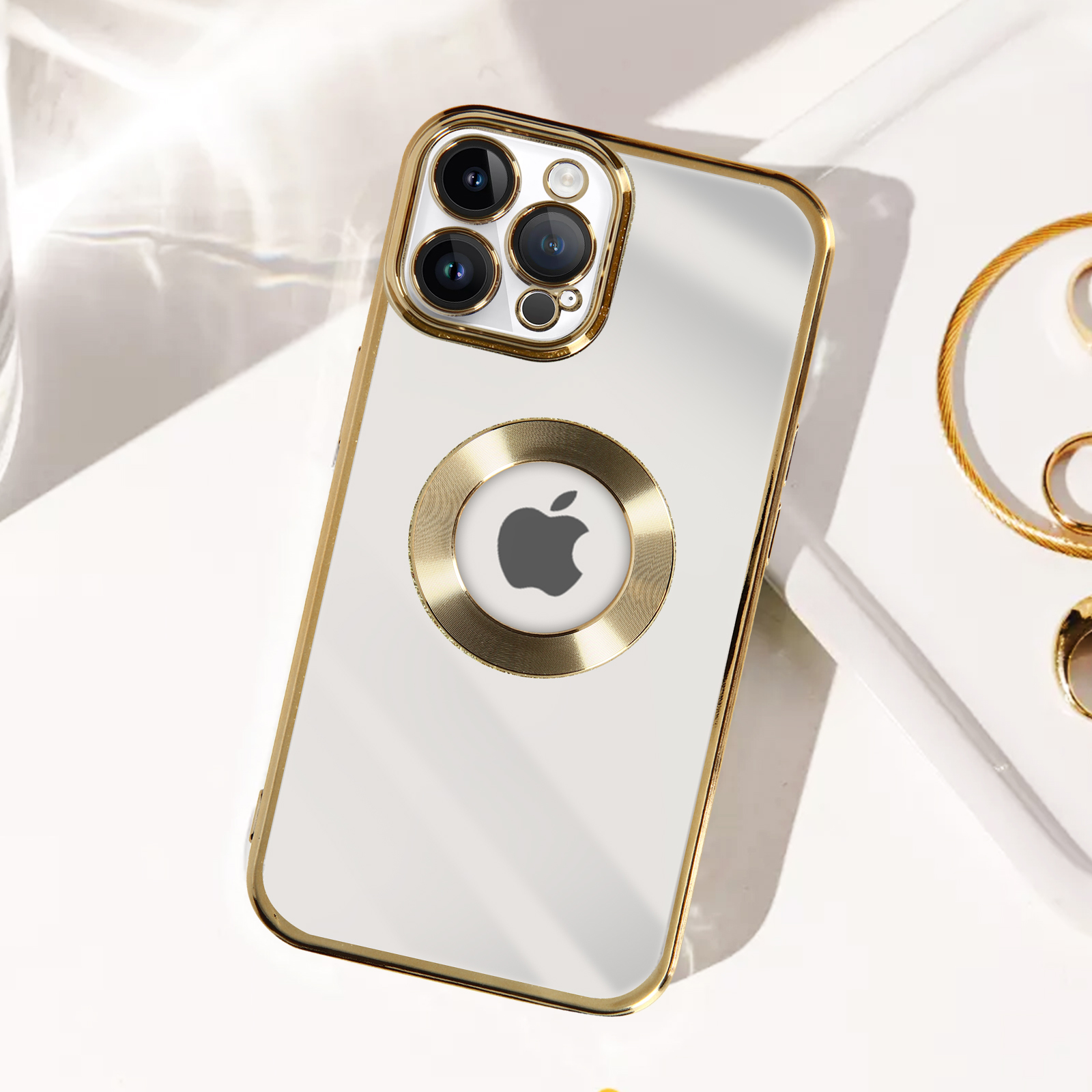 Custodia bianca con cornice dorata e logo Apple. Bracciale dorato sullo sfondo.