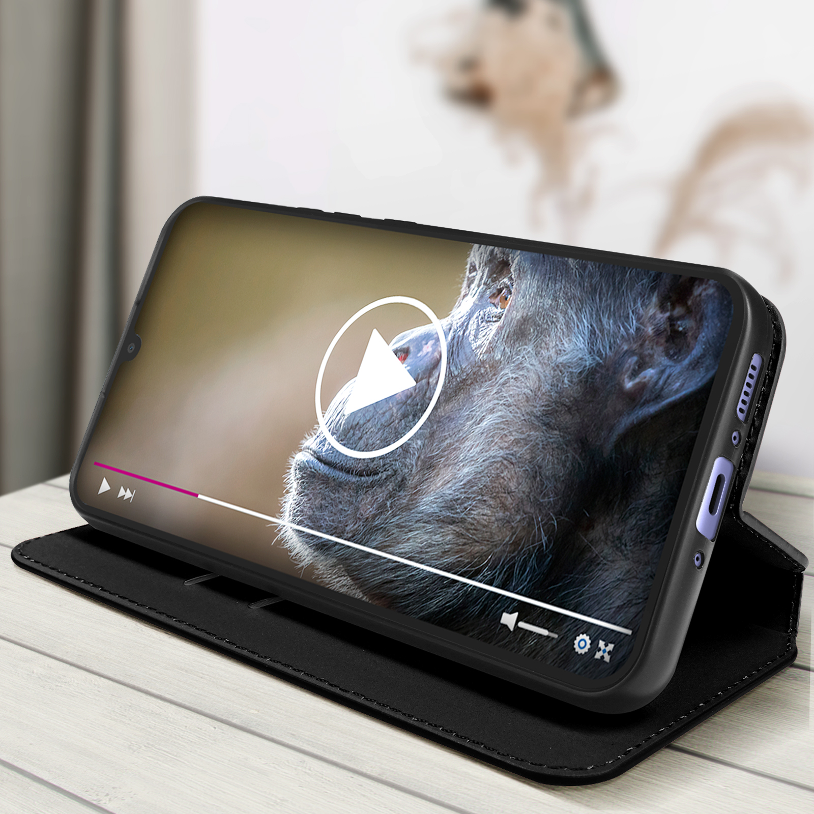 Telefono nero in una custodia nera, mostra il video di uno scimpanzé. Il telefono è su un tavolo di legno.