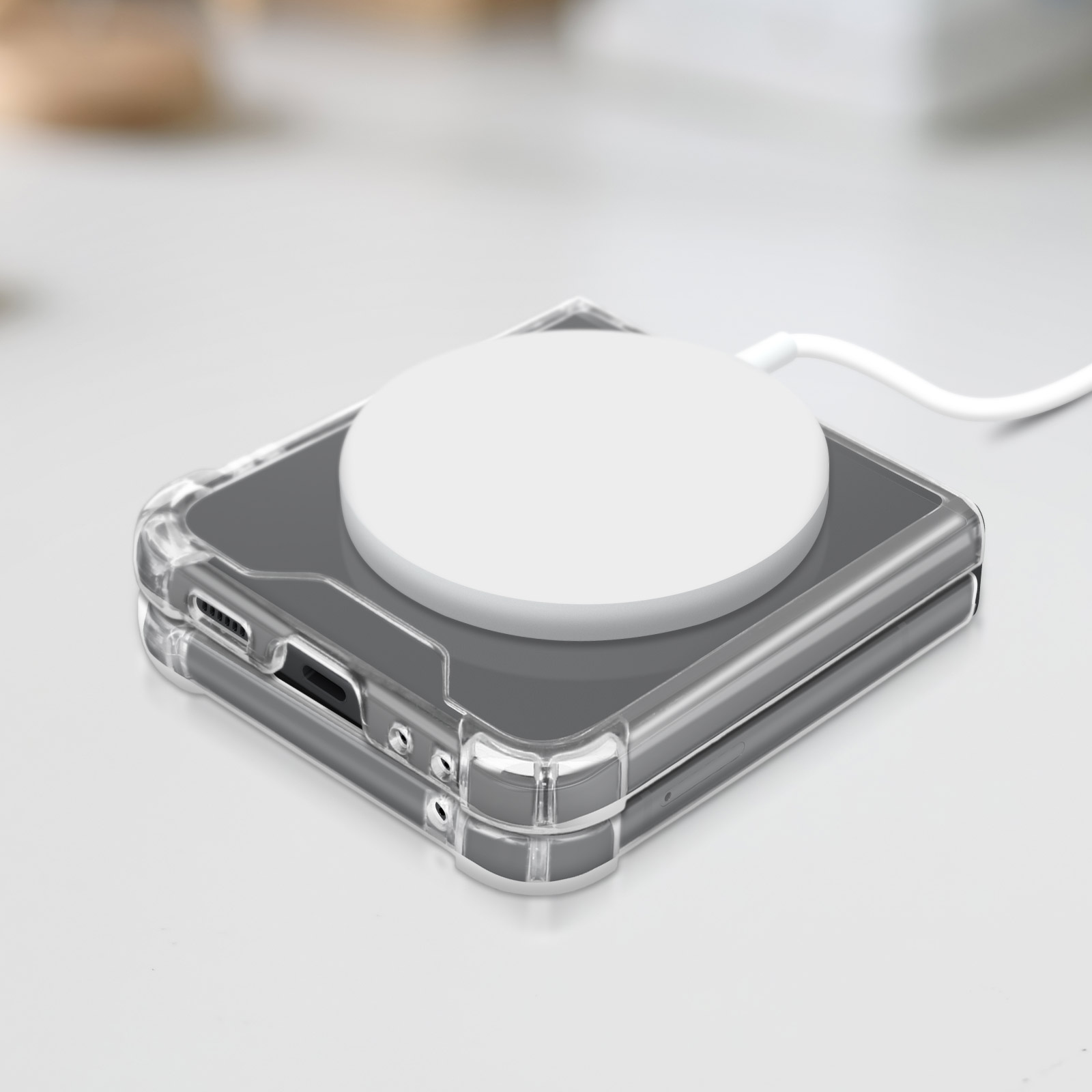 Un chargeur sans fil blanc sur un téléphone gris, dans une coque transparente. Câble blanc branché. Arrière-plan flou.