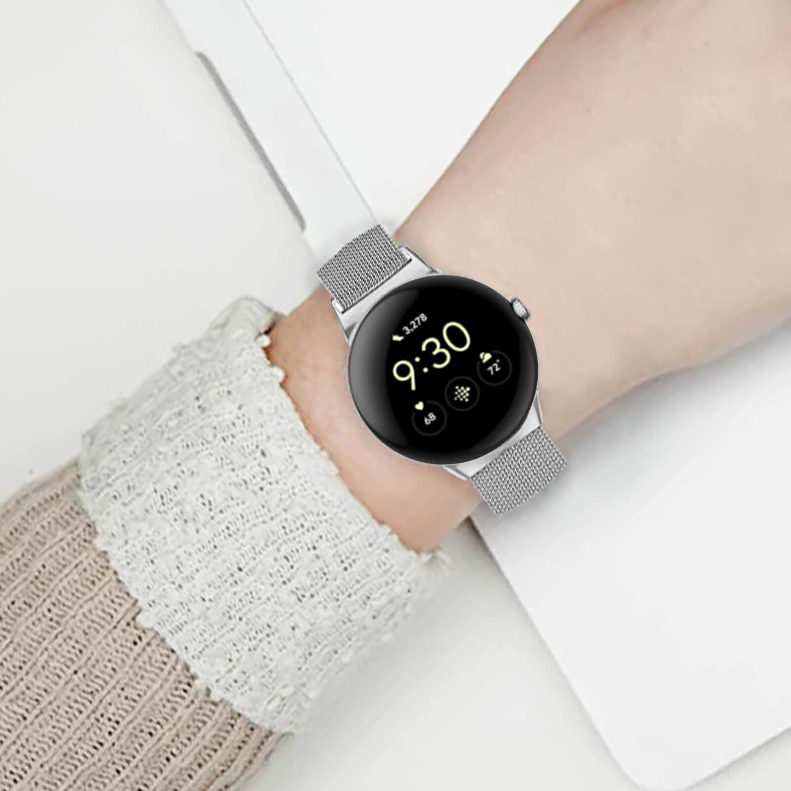 Smartwatch plateado en muñeca, mostrando hora, fecha y batería, en un portátil.