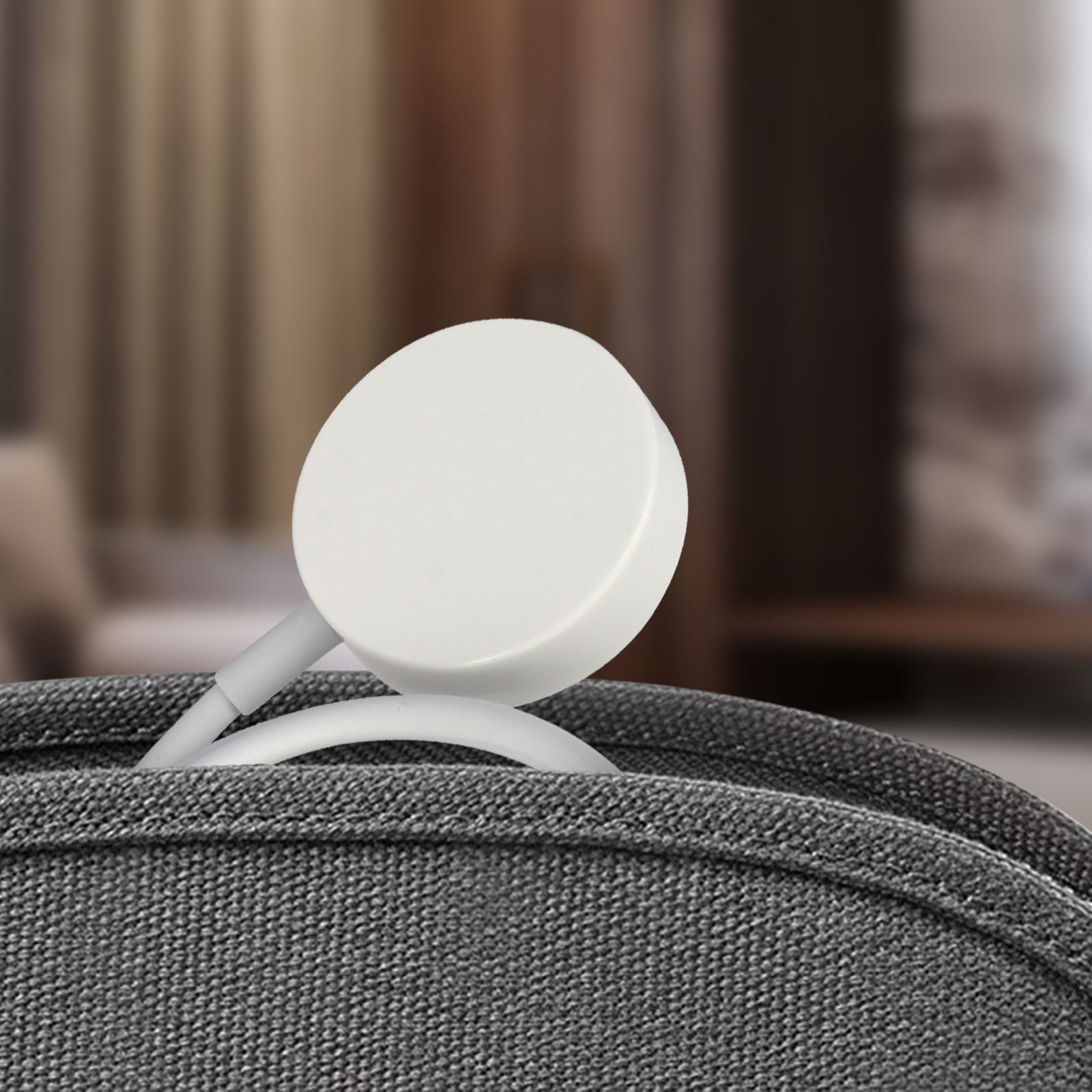 Weißes Smartwatch-Ladegerät in einem grauen Beutel. Der Hintergrund ist unscharf.