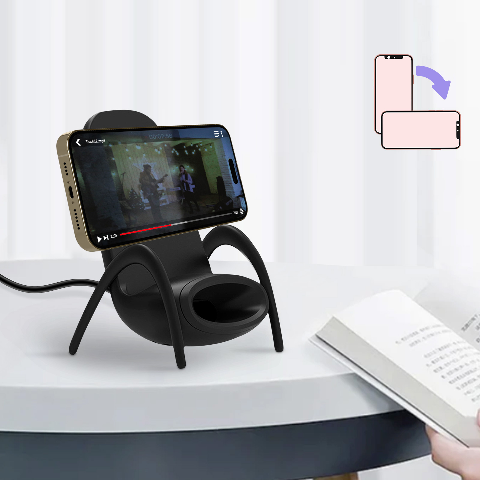 Un teléfono en un soporte muestra un video. Un libro está en la mesa.